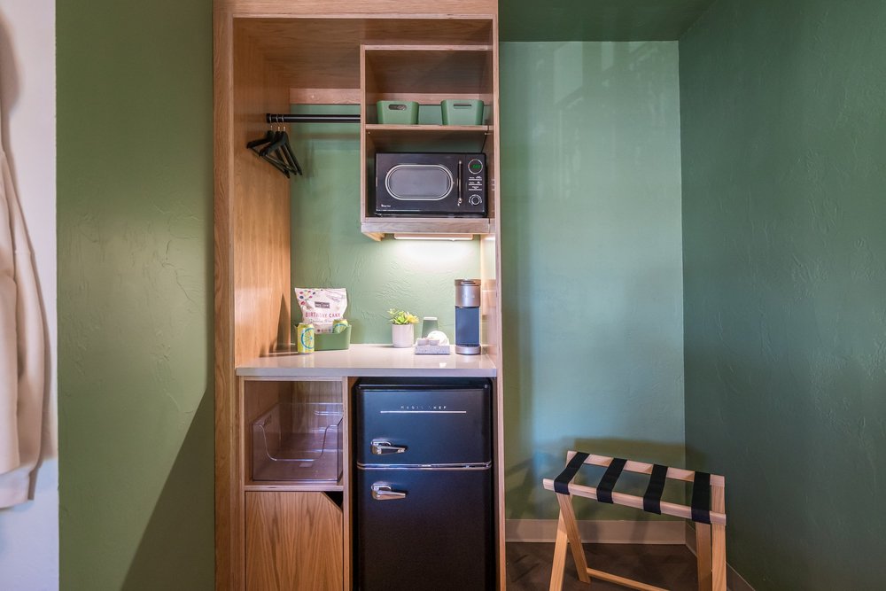 A green-painted closet nook with wood shelving, a microwave and a black mini fridge