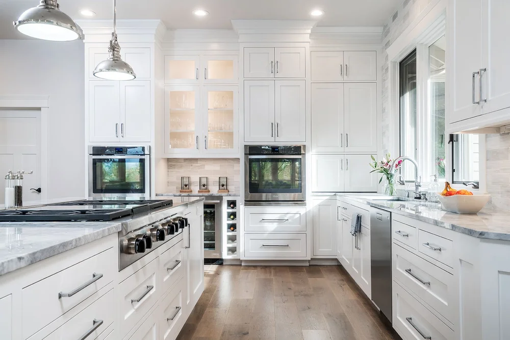 White kitchen with inset cabinetry to the ceiling, glass-front uppers, marble counters and polished nickel pendants
