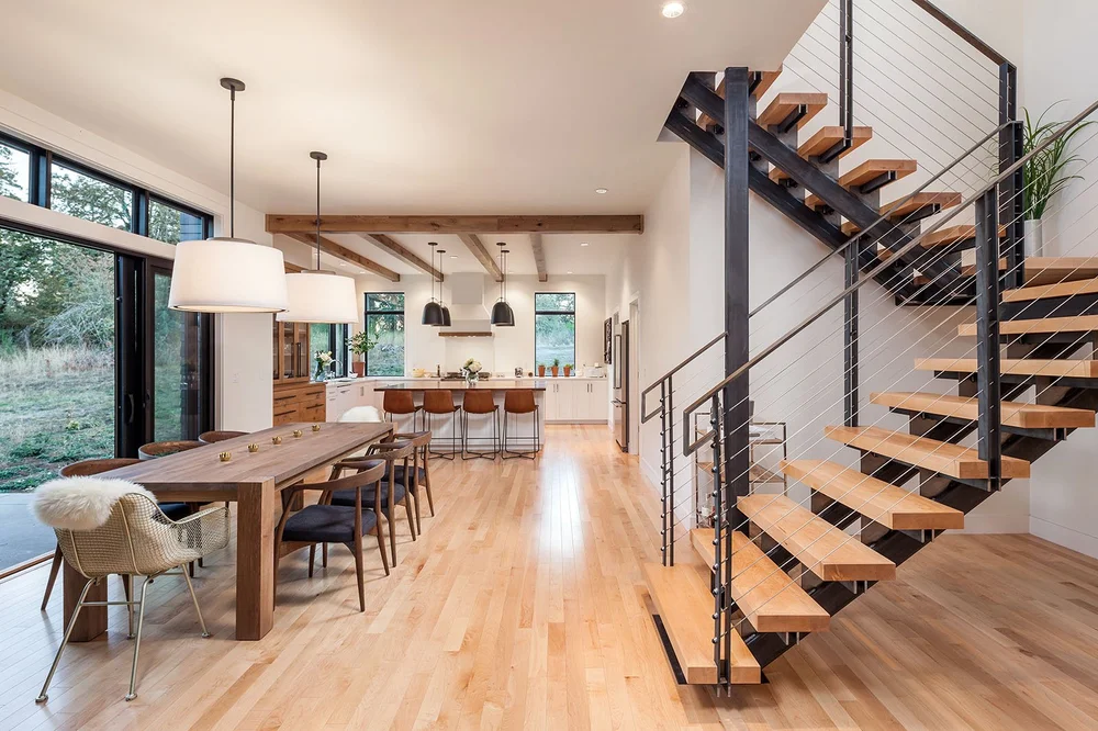 Open dining room and kitchen under timber beams, with a floating steel and maple stair