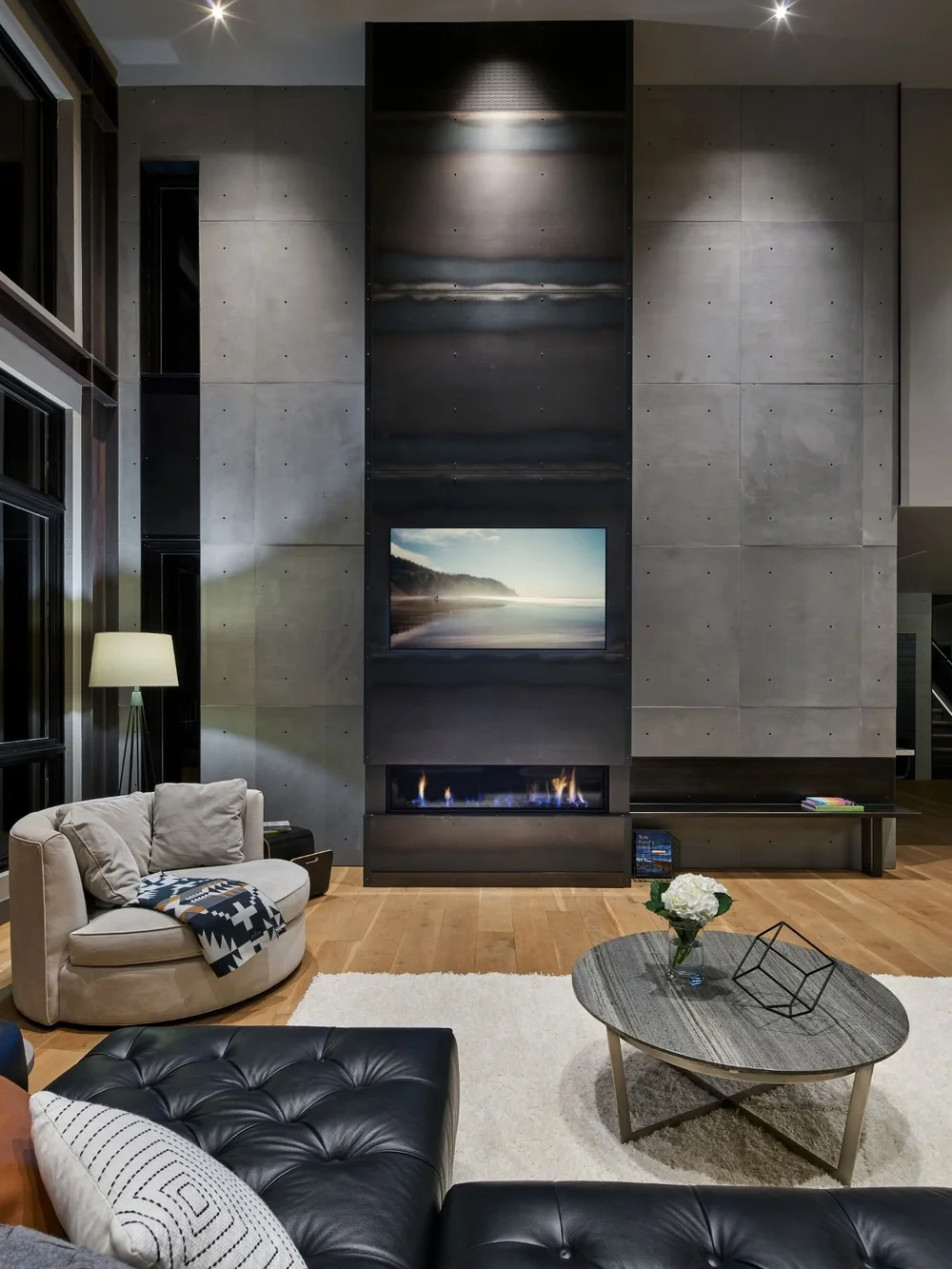 Blackened steel fireplace surround set into a wall of concrete panels, lit from above