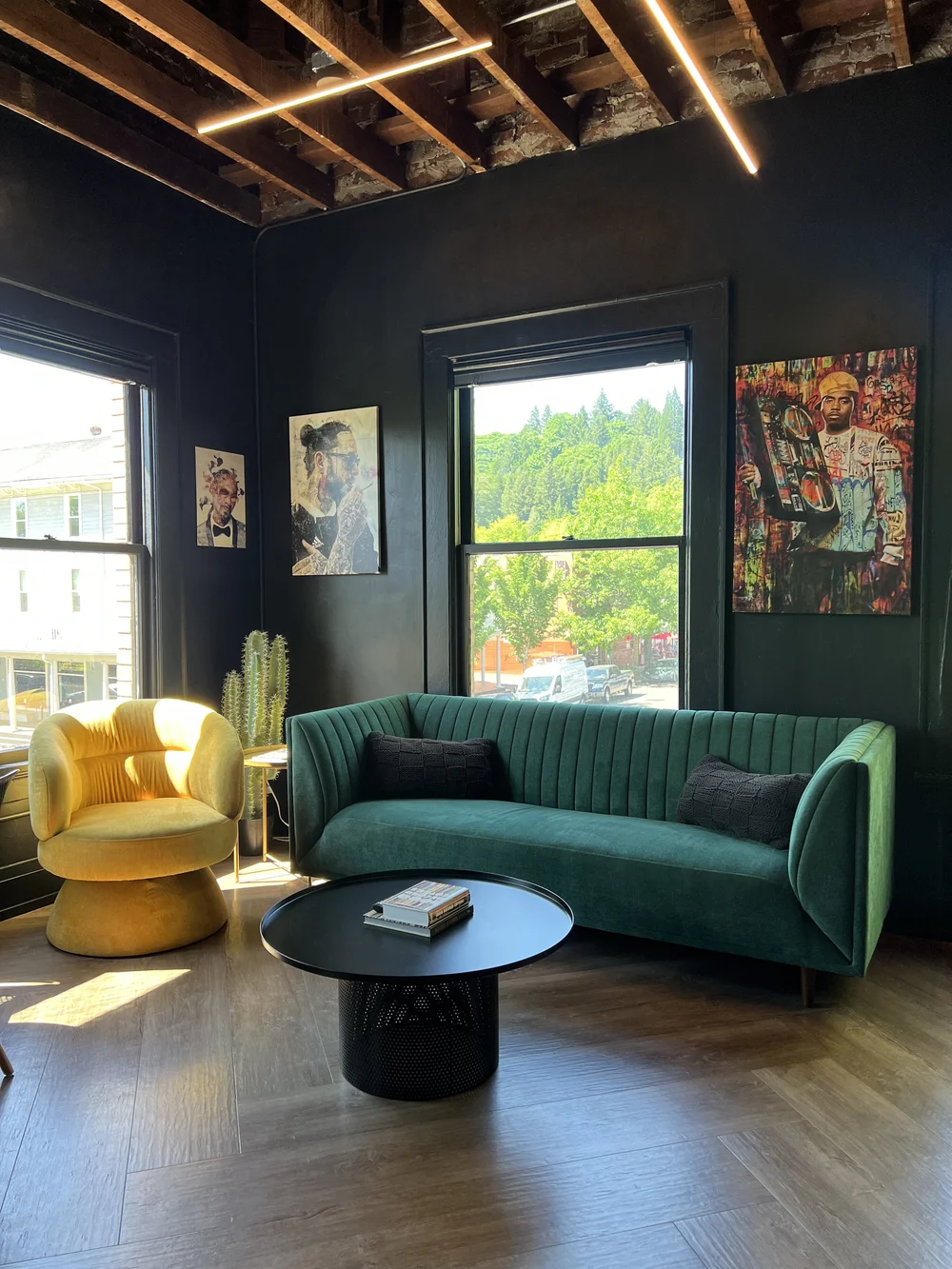 Dark lounge with a green velvet sofa, a yellow chair and exposed ceiling joists