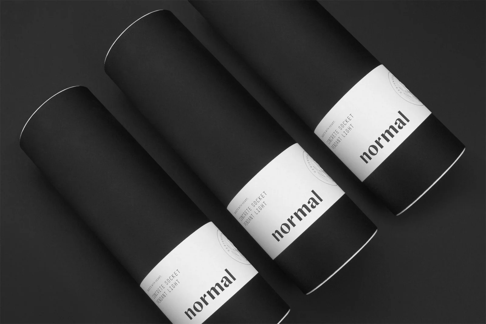 Trois tubes de carton noirs, emballages (packagings) réalisés par Figure studio de branding pour la marque Normal.