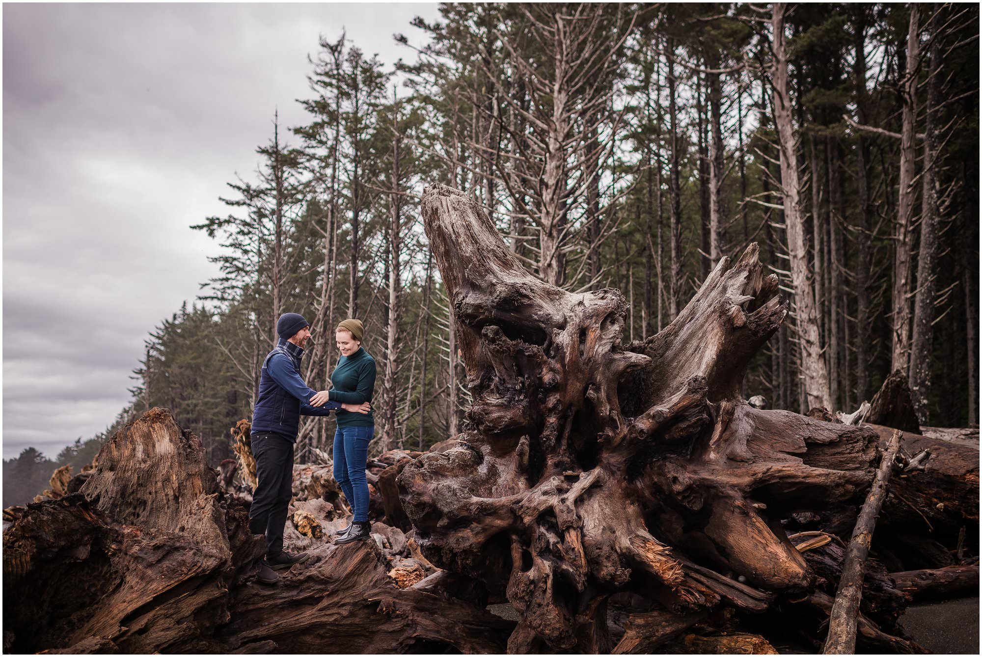  A couple exploring large broken trees on a beach in Washington State for their destination wedding.  