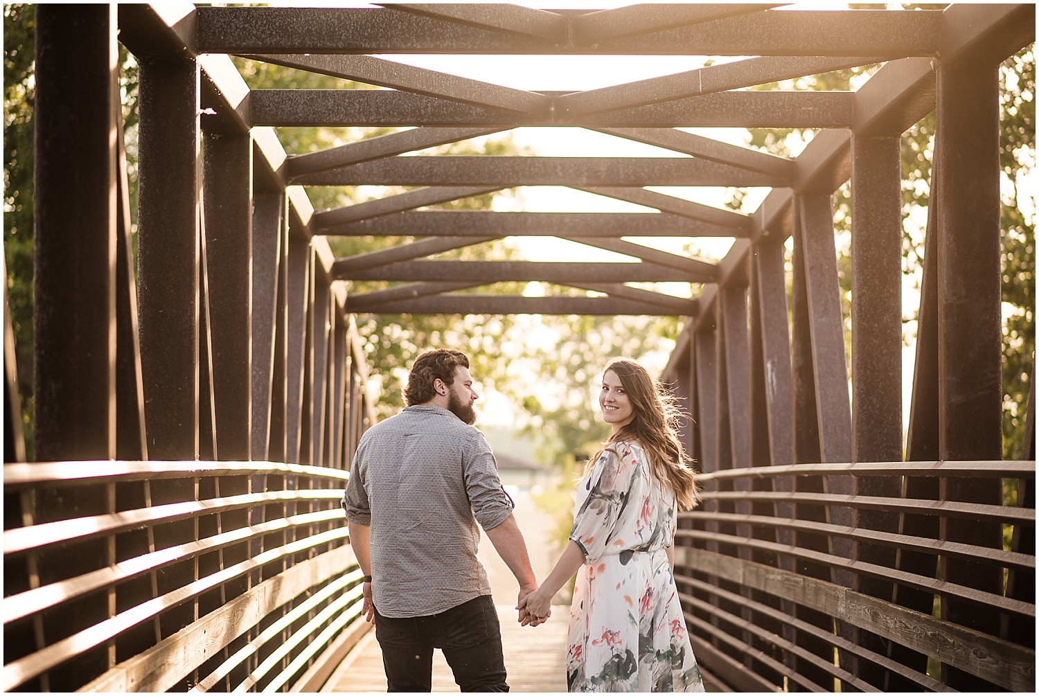  A woman looking back at the camera while she and her partner walk down a bridge in a park.  