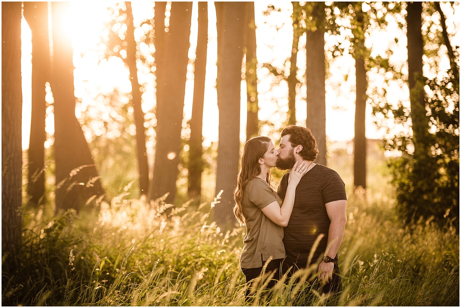  A casually dressed couple kissing on a beach near sunset.  