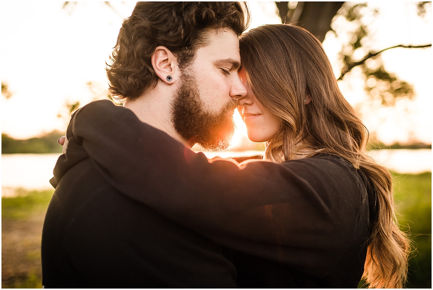  A close-up photograph of a couple embracing with the sun glowing between their faces.  