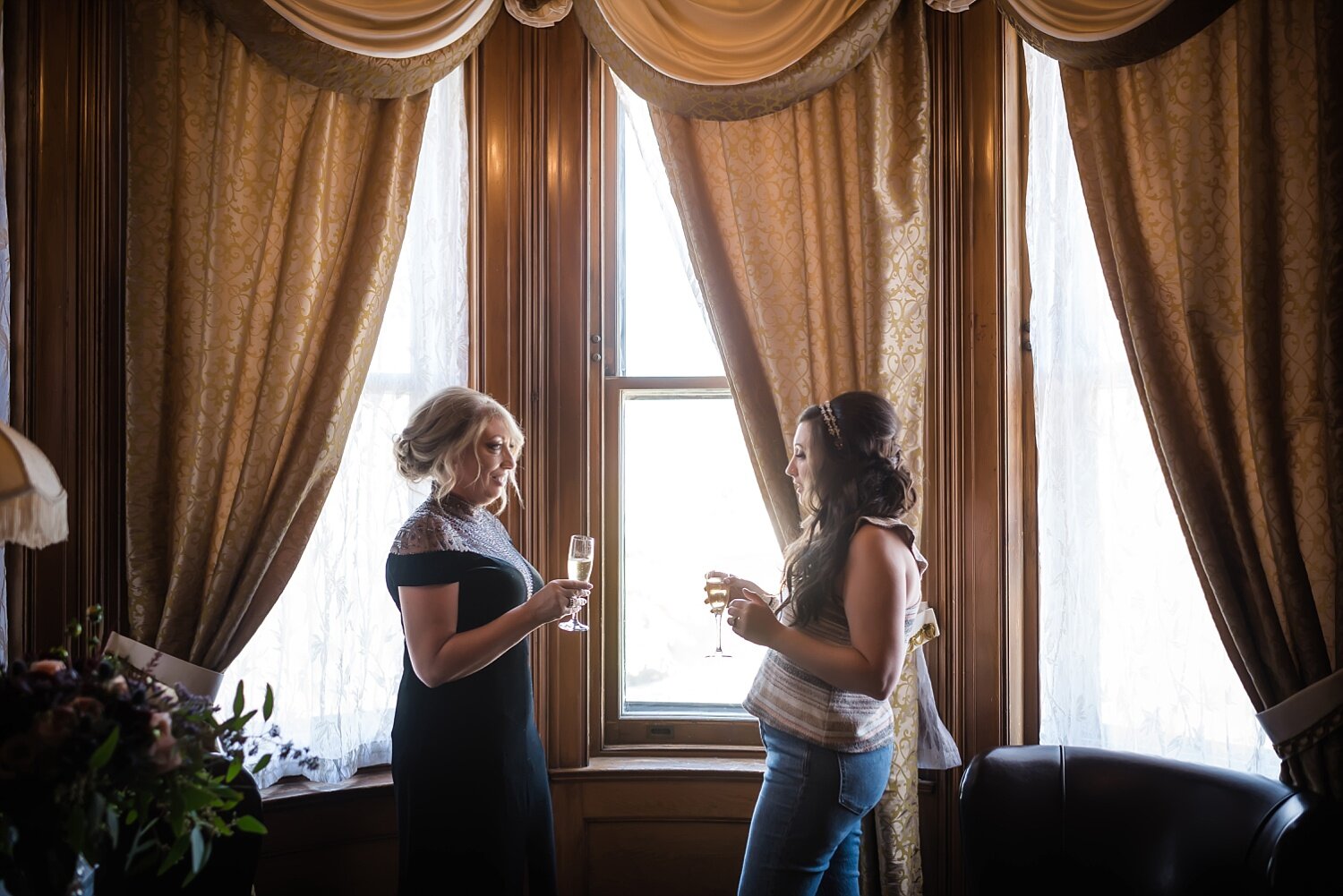  A bride and her mom share a toast in front of a large historic window before the bride gets dressed.  