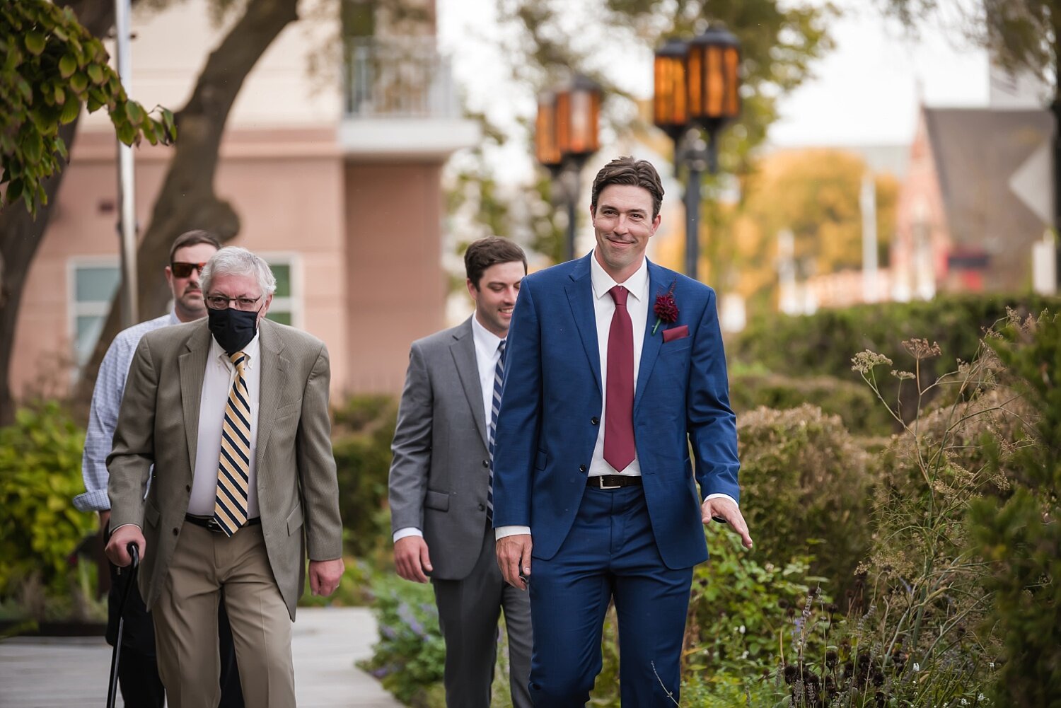  A groom wearing a blue suit and red tie walks down the aisle before his wedding.  