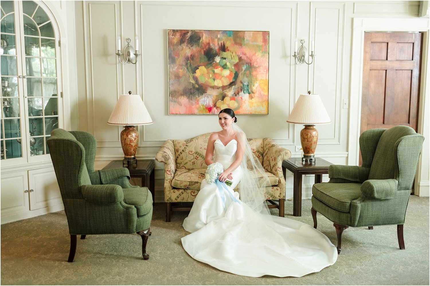  A happy bride sits and talks with her bridesmaids in front of art in a historic wedding venue.  
