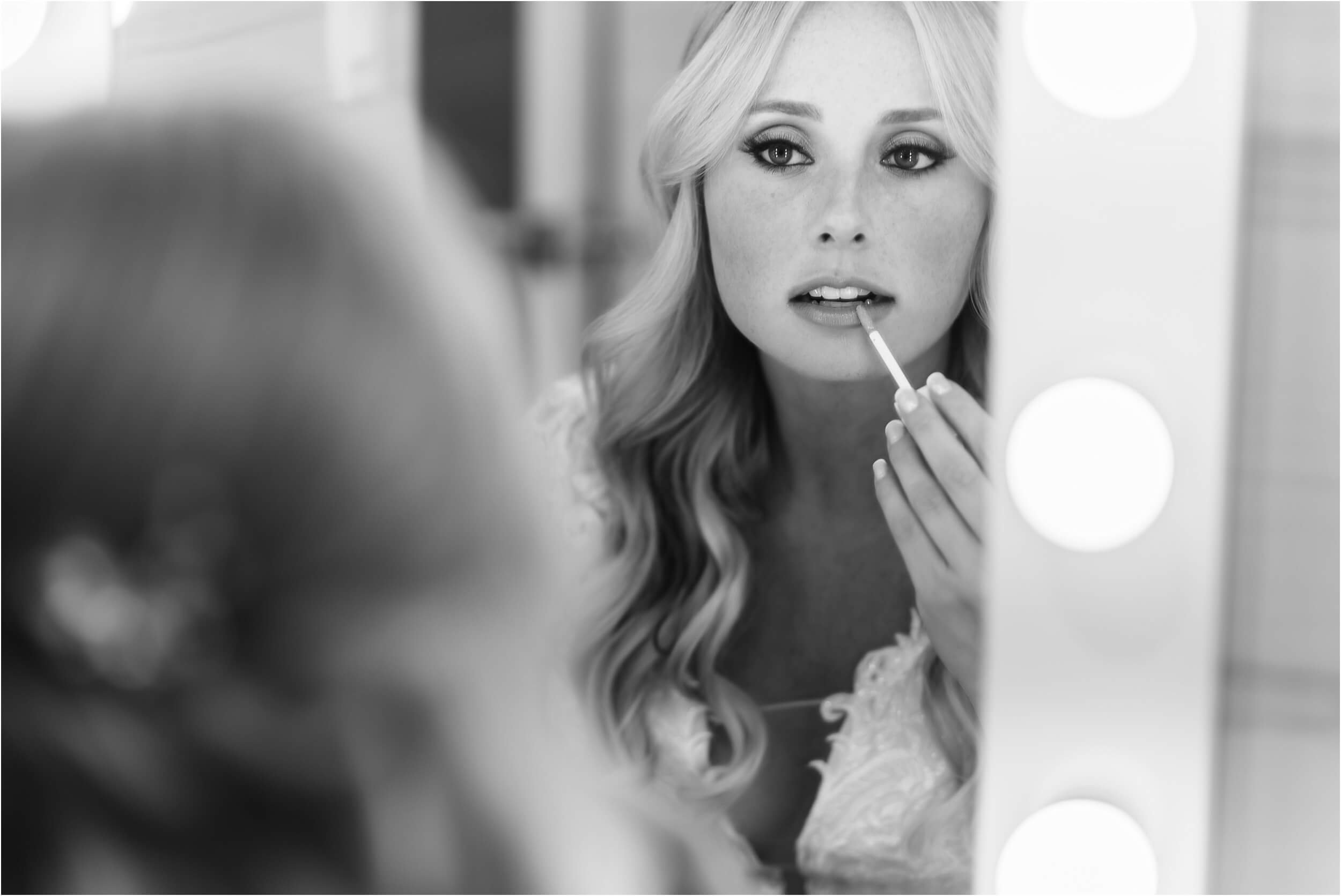  A beautiful bride applies her lipstick in a lighted mirror in the bathroom of her hotel.  