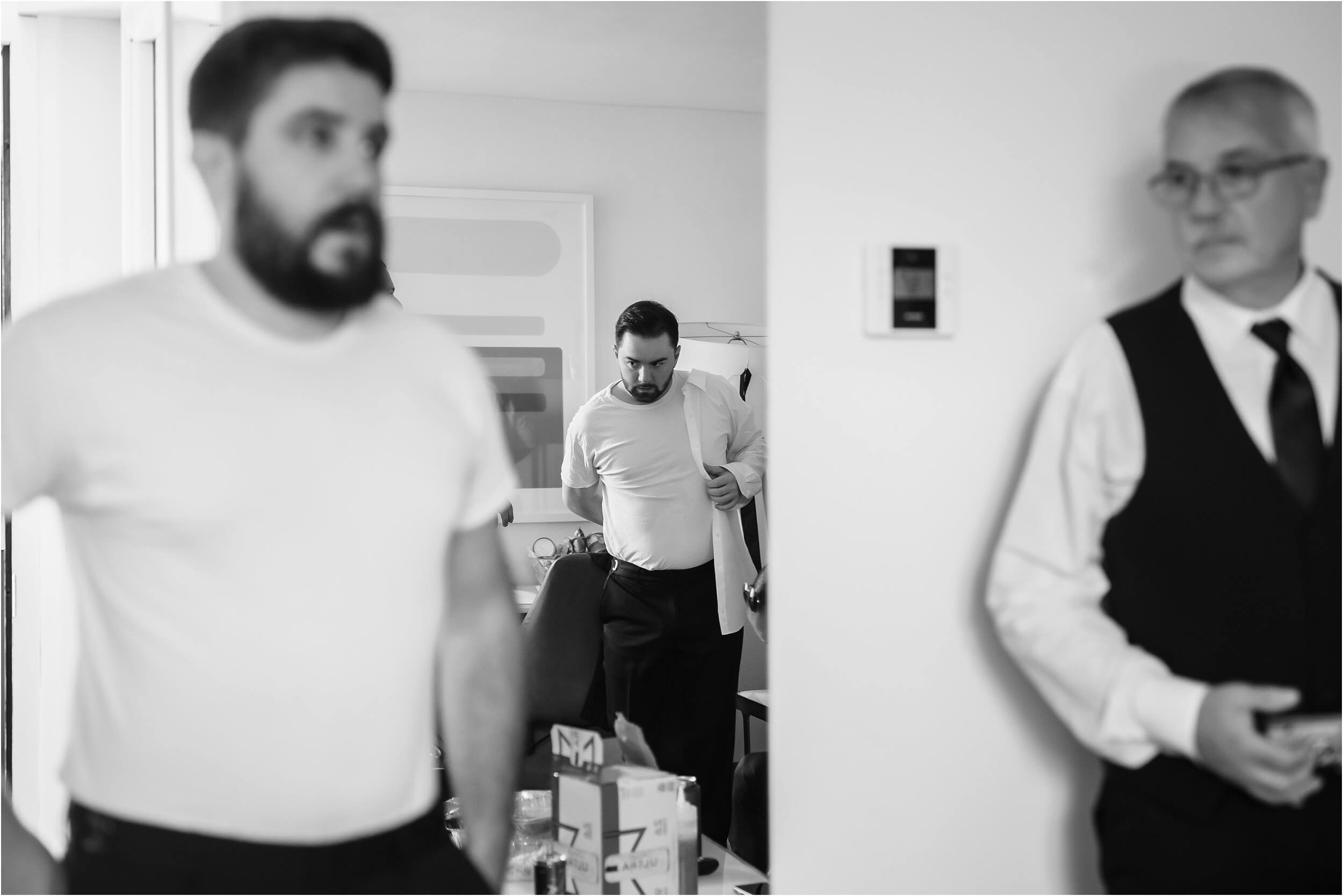  A groom, his dad, and his groomsmen help each other get dressed.  