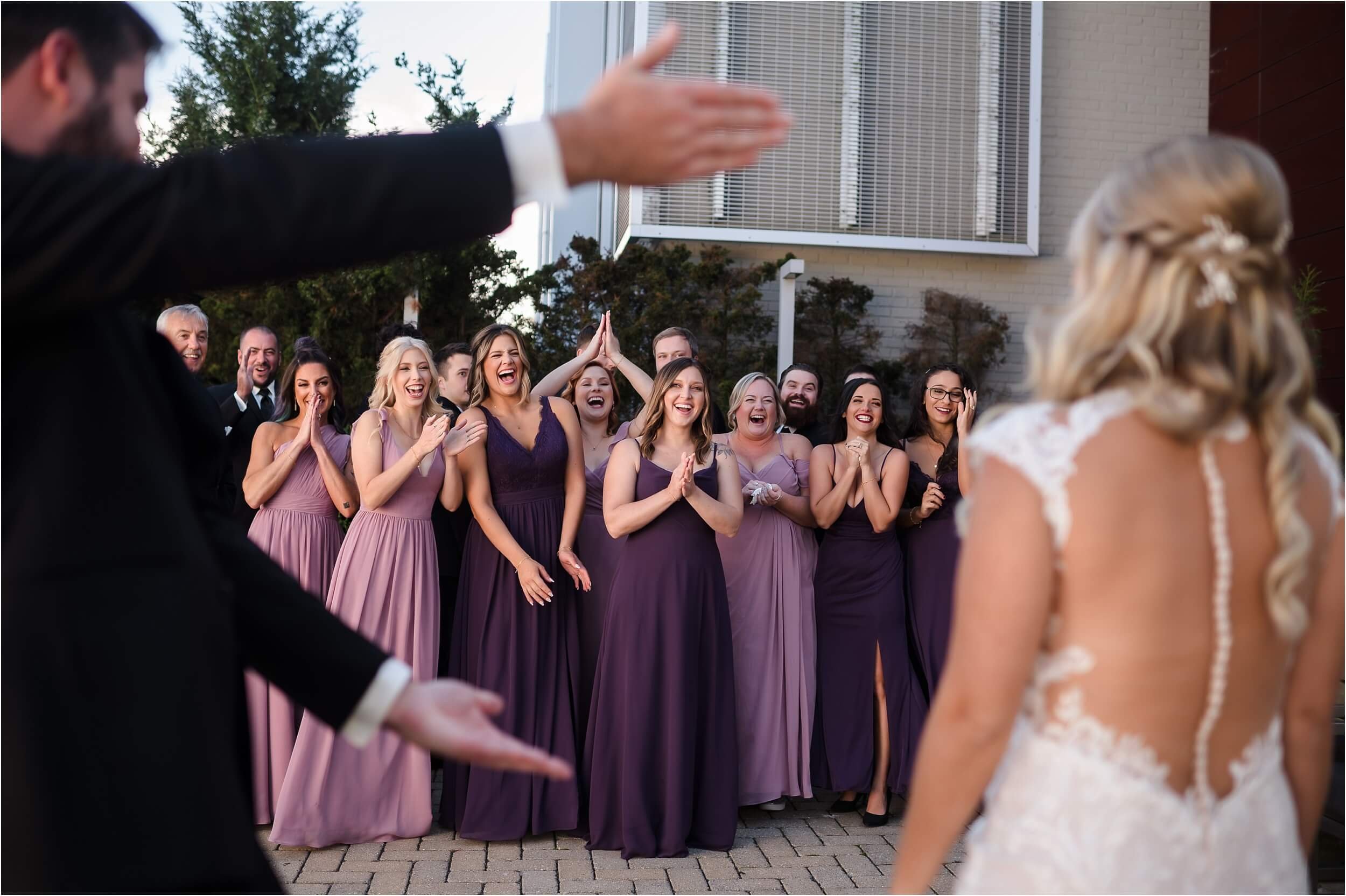  Bridesmaids wearing pink and purple dresses react joyfully to their friend who is getting married.  