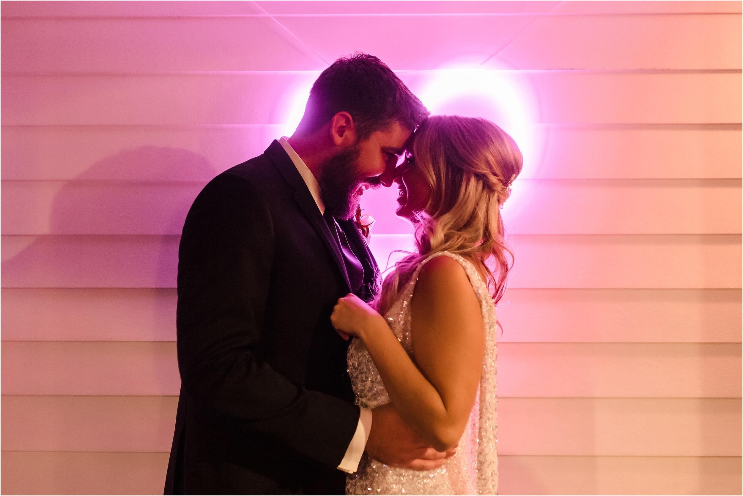  A couple embraces in front of a heart neon sign at their wedding reception.  