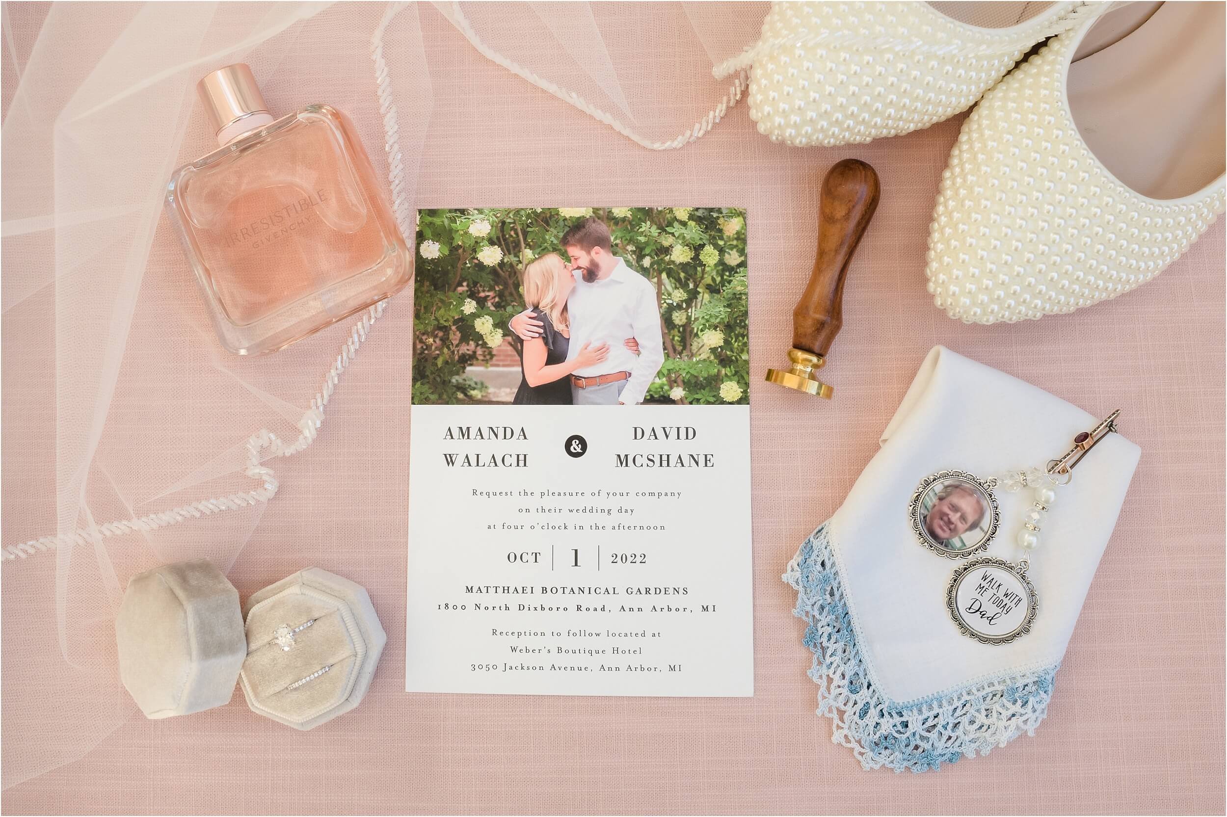  A pink and white layflat of wedding details including shoes, an invite, perfume,  and family mementos.  