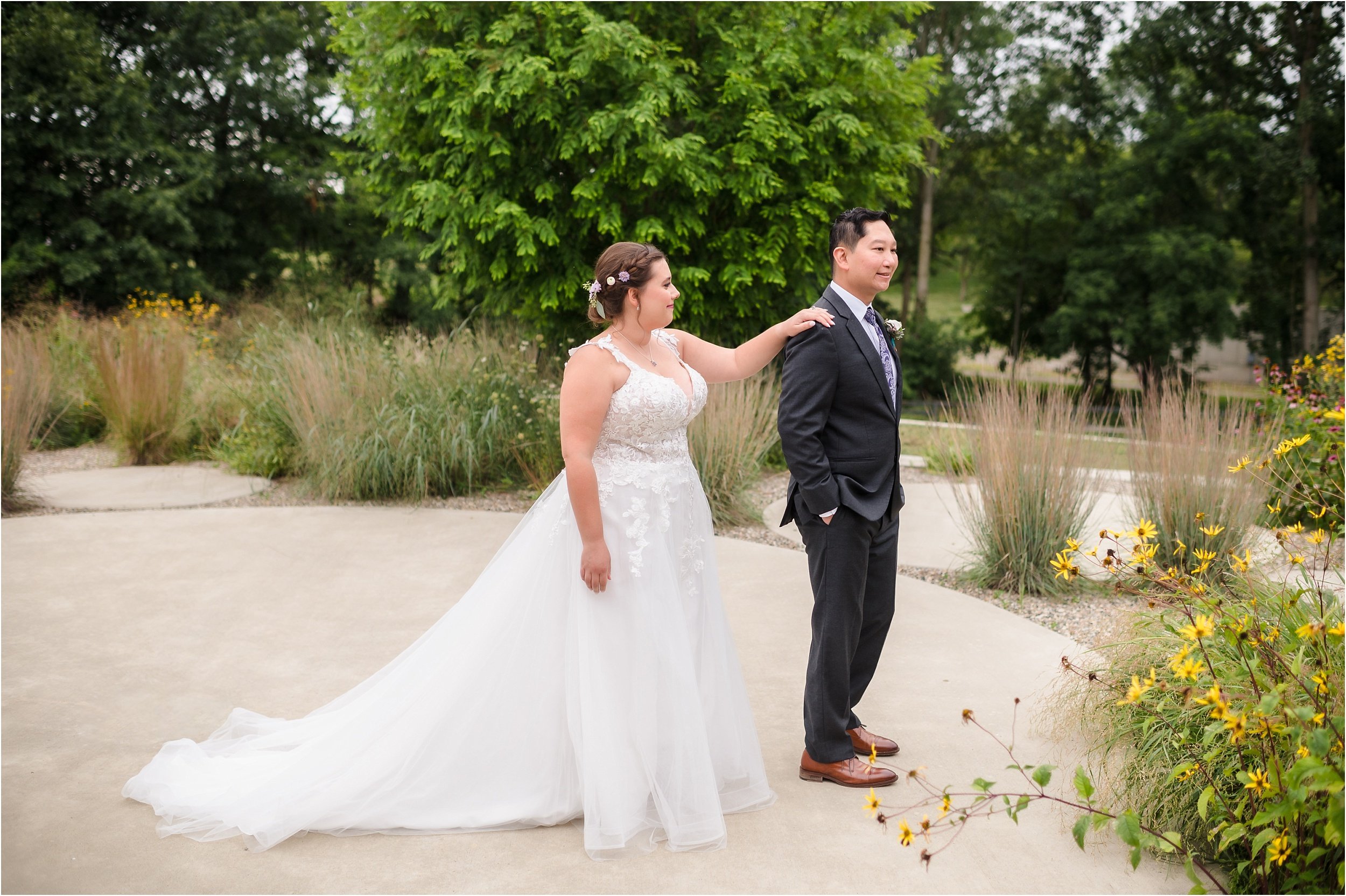  A bride wearing a long wedding dress taps her fiance on the shoulder while they see each other for the first time on their wedding day.  