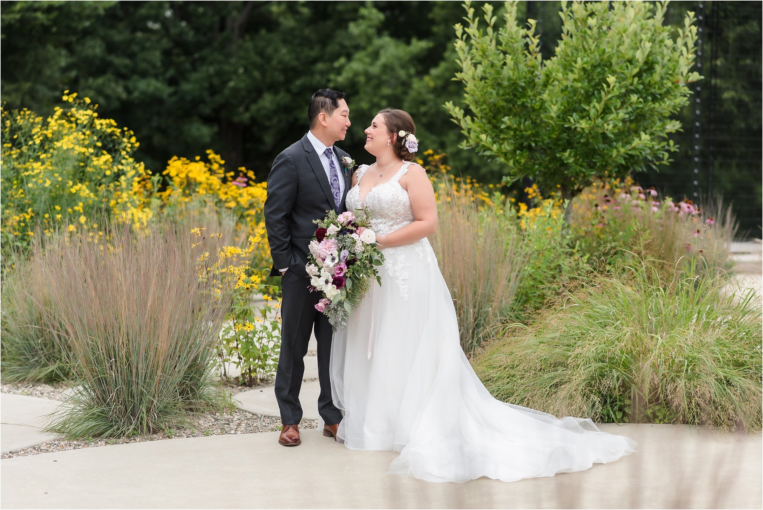  A couple looks at each other in a wildflower garden on a cloudy wedding day.  