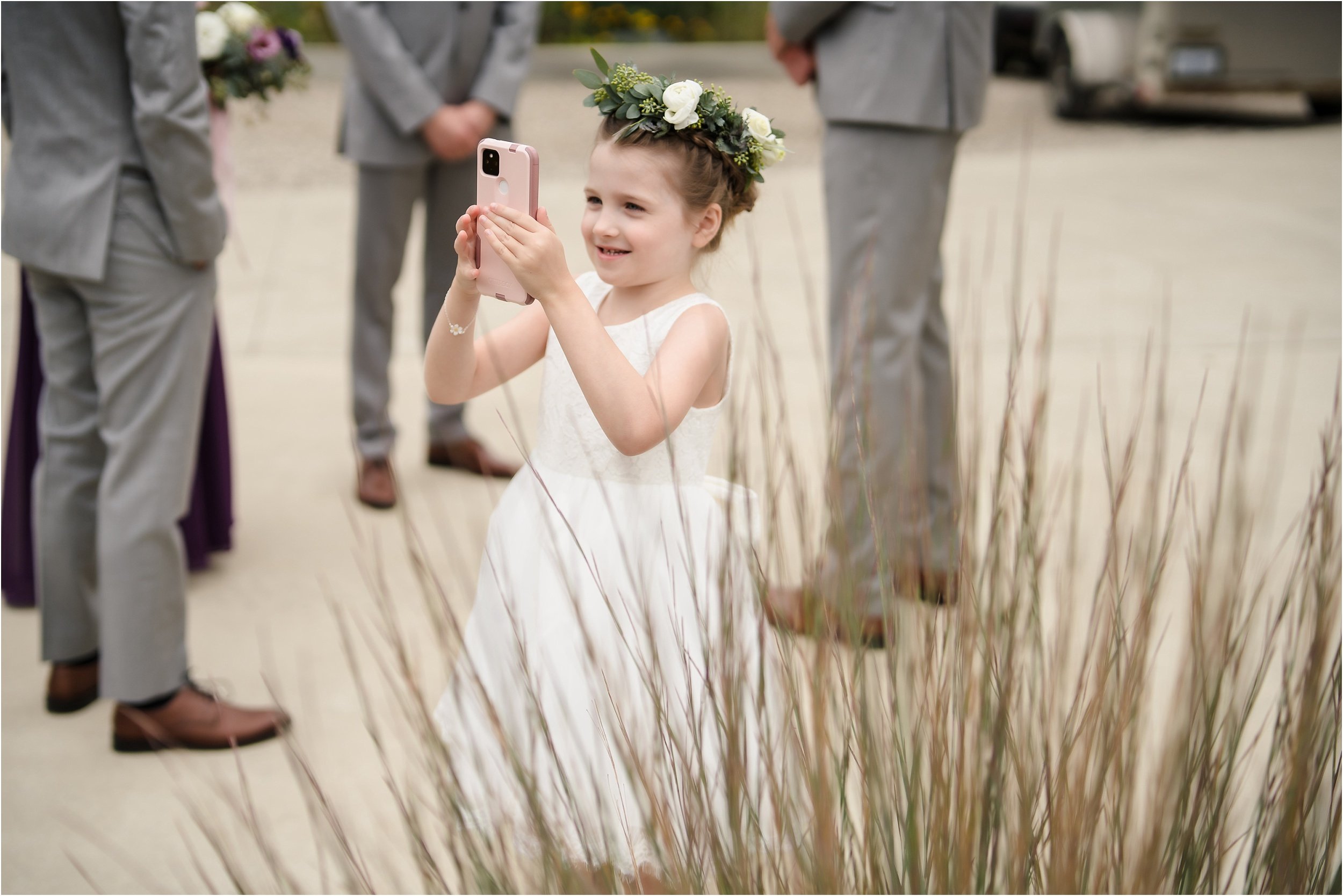  A flowergirl takes a cell phone photo during portraits on a wedding day.  