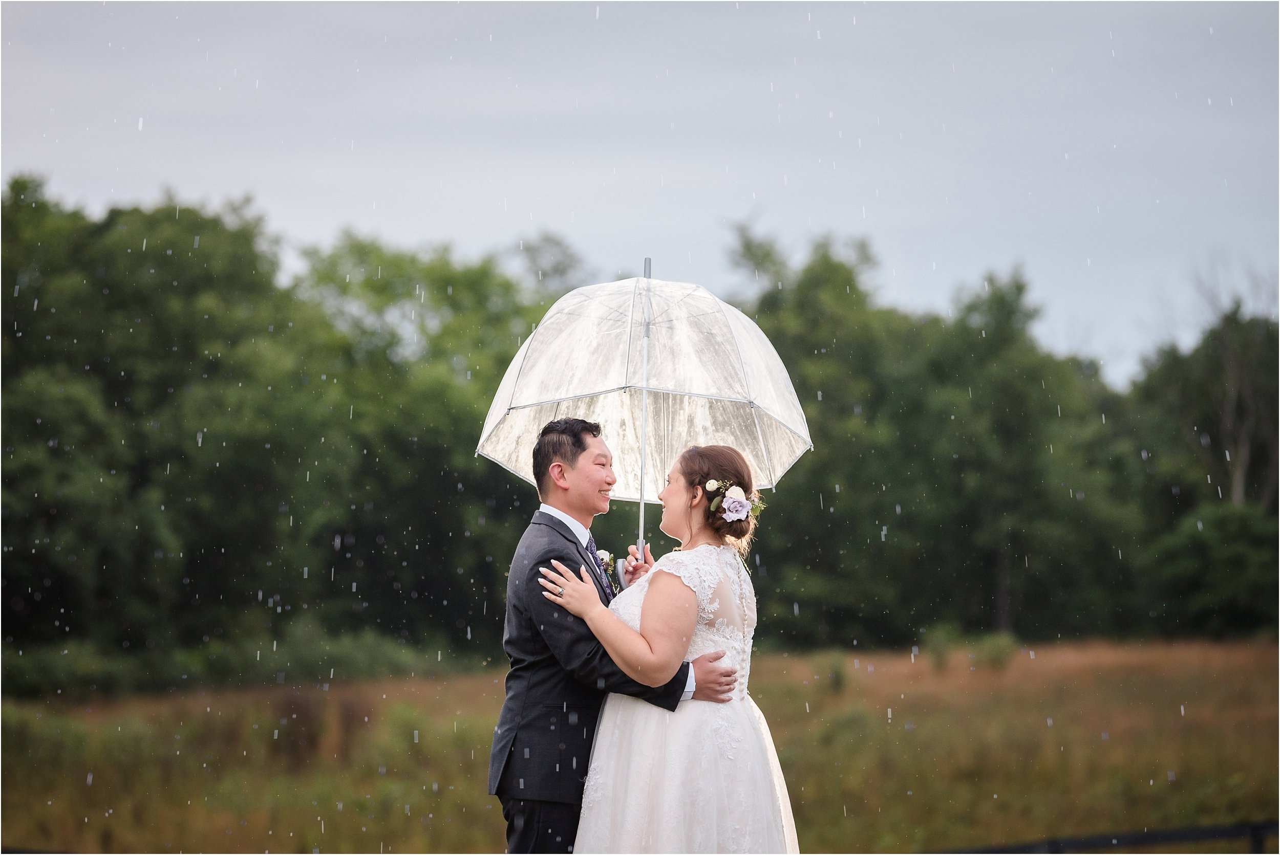  A couple sharing a moment under a umbrella at sunset after their rainy wedding day.  