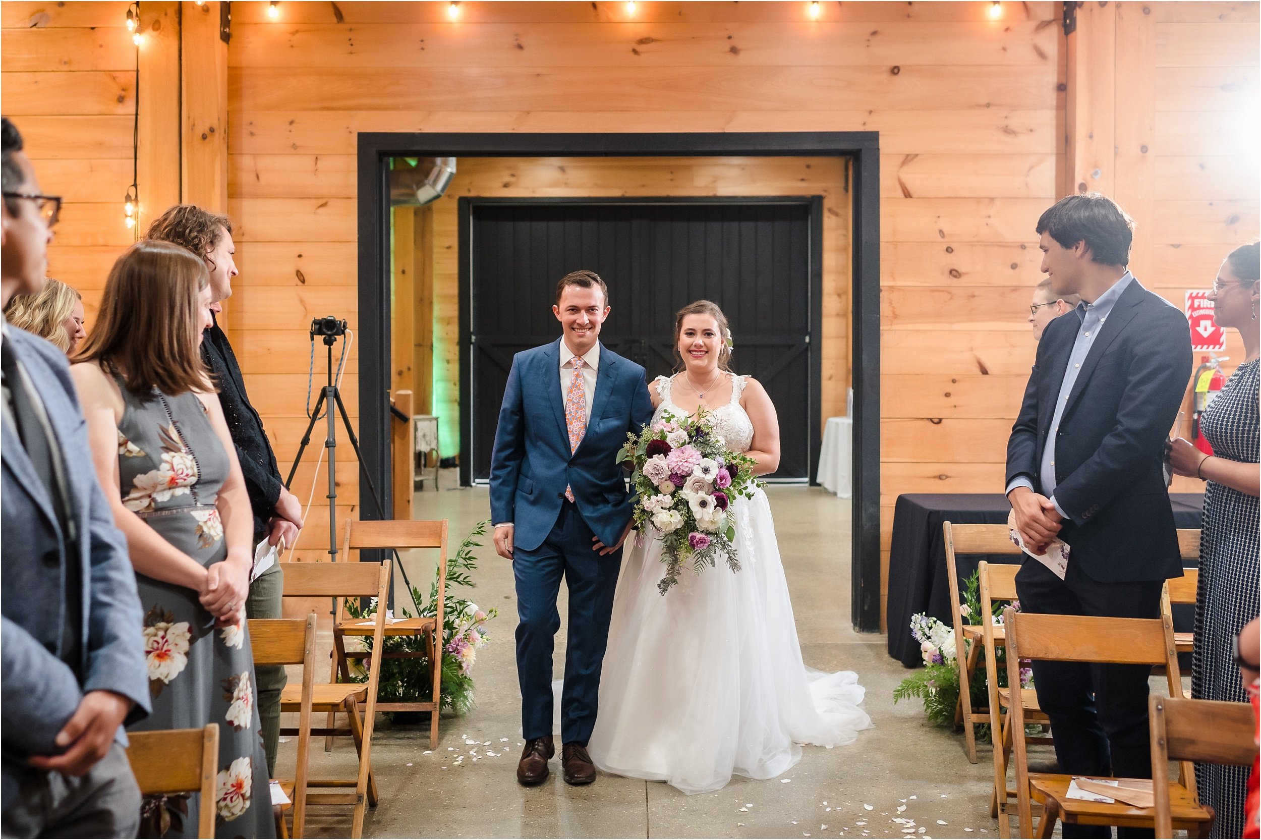  A smiling bride walks down the aisle with her brother.  