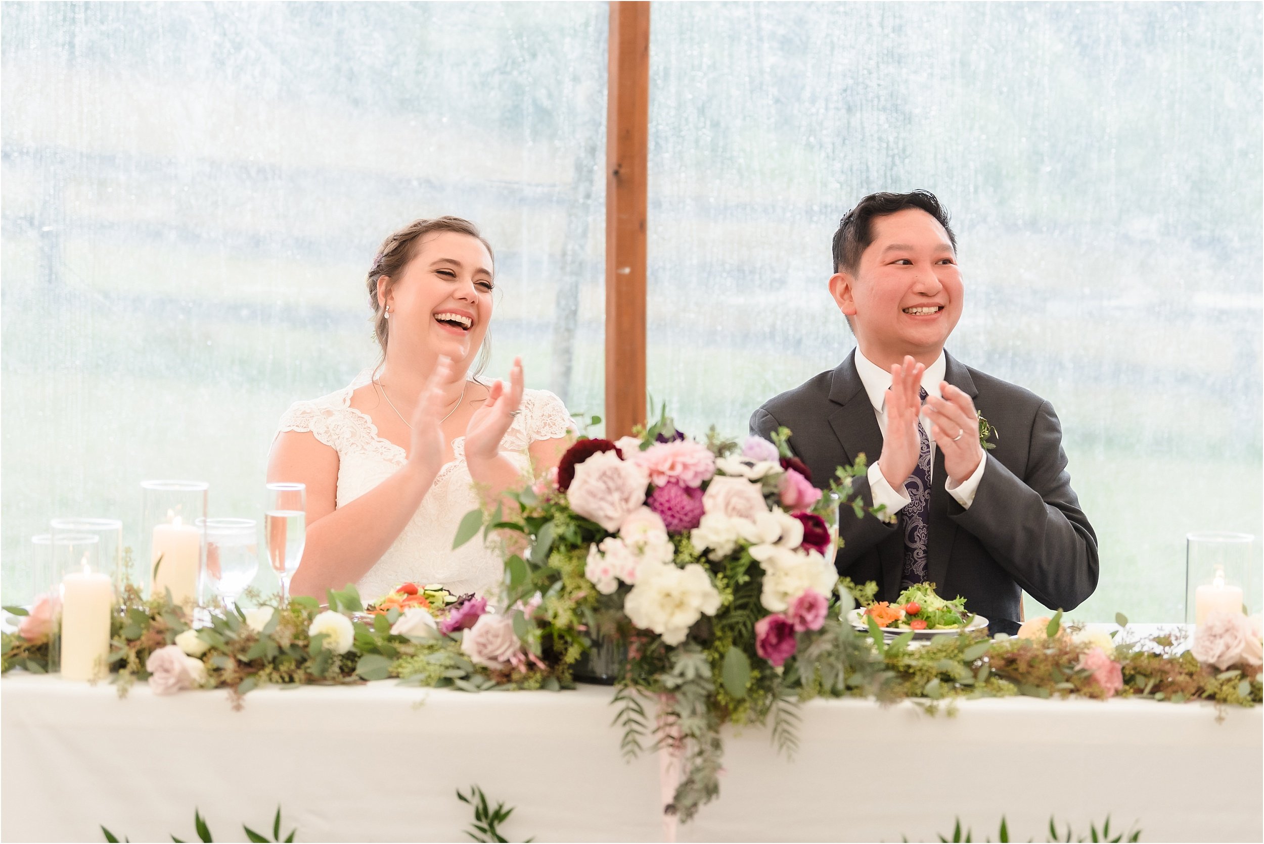  A man and woman laugh and clap following a toast from a groomsman.  