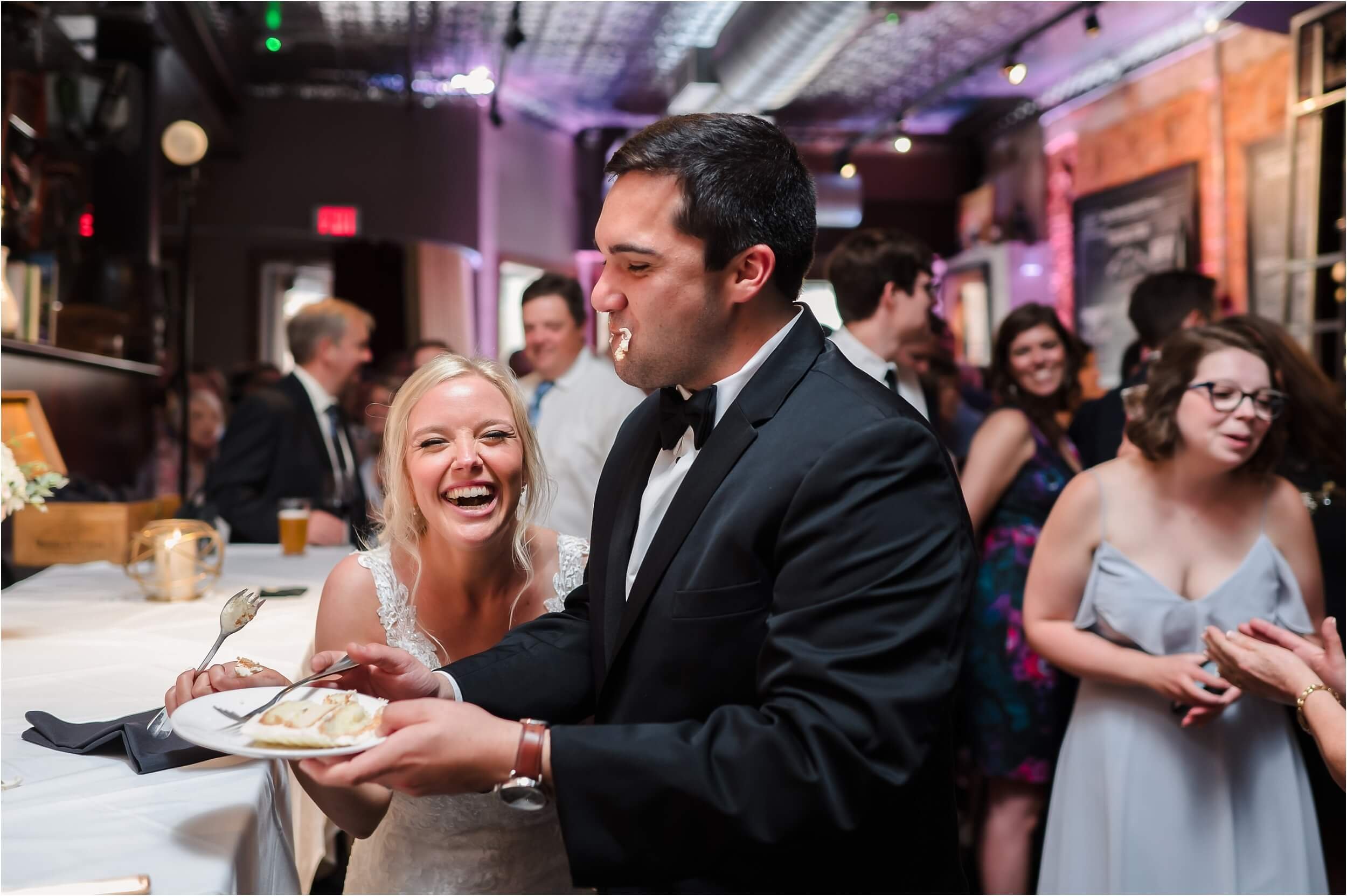  A bride laughs towards the camera after accidentally getting cake on the groom’s face.  