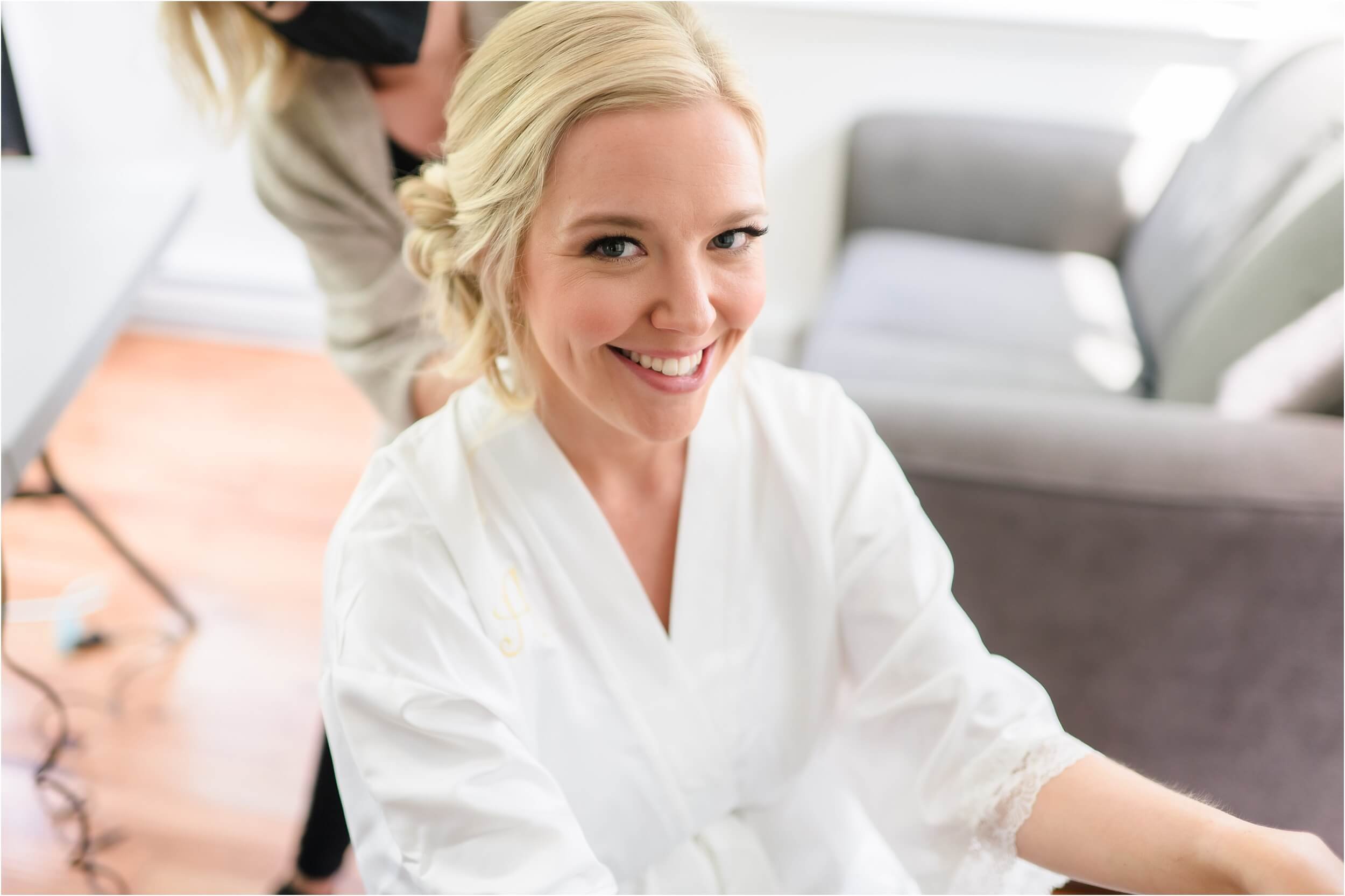  A blonde bride smiles at the camera while getting her make-up done.  