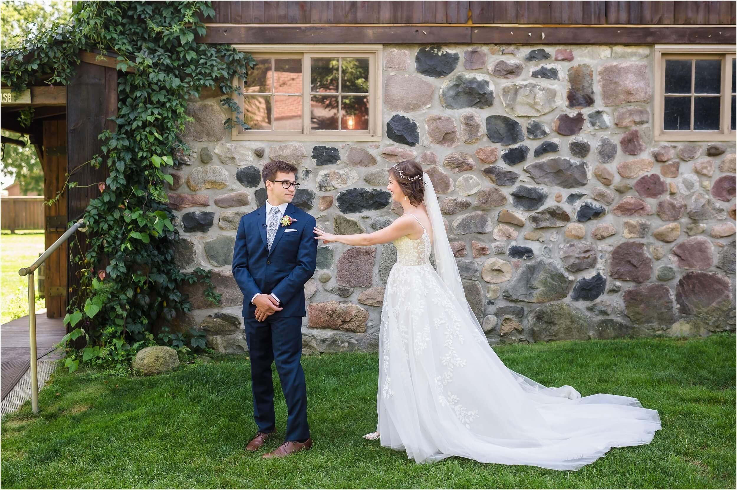  A bride sneaks up behind her husband before their wedding in front a historic barn venue in Michigan.  