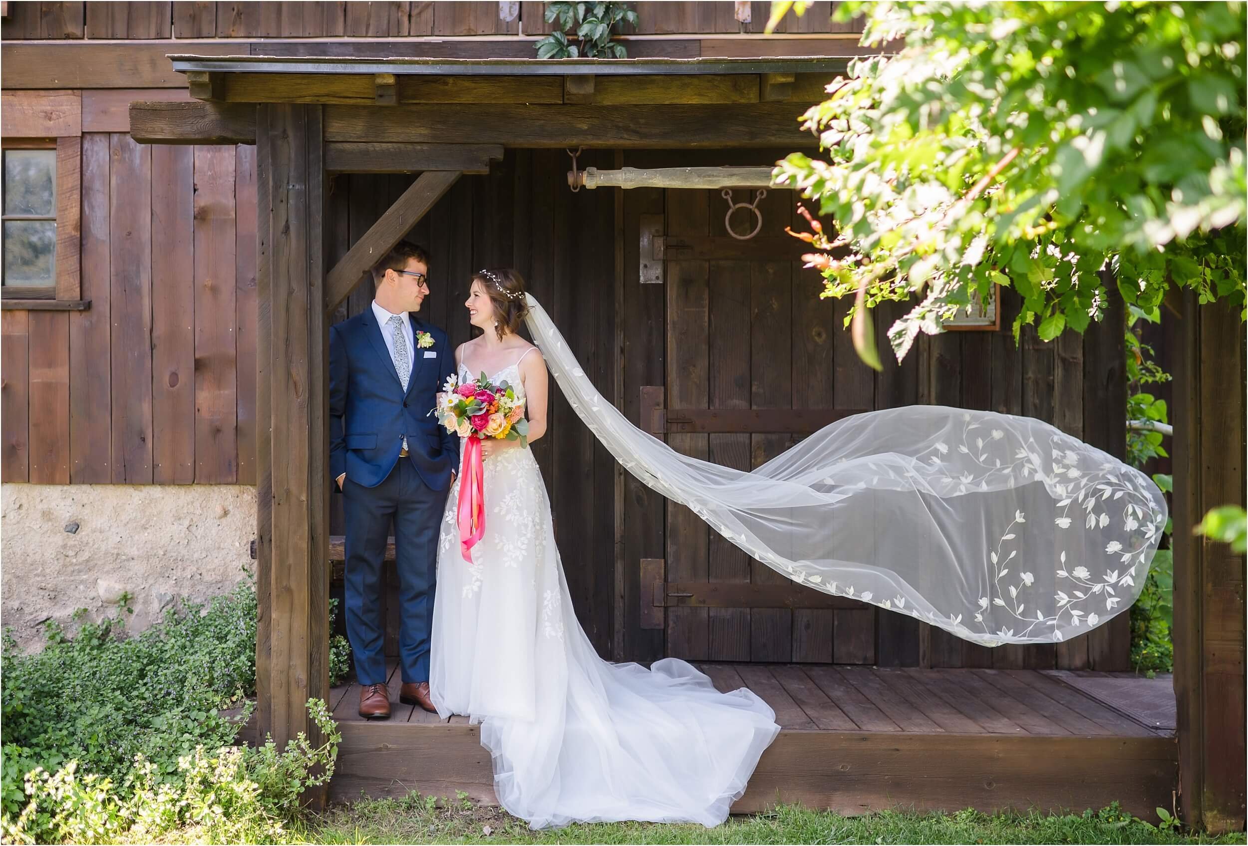  A gust of wind picks up a brides floral embroidered veil while she and her partner talk.  