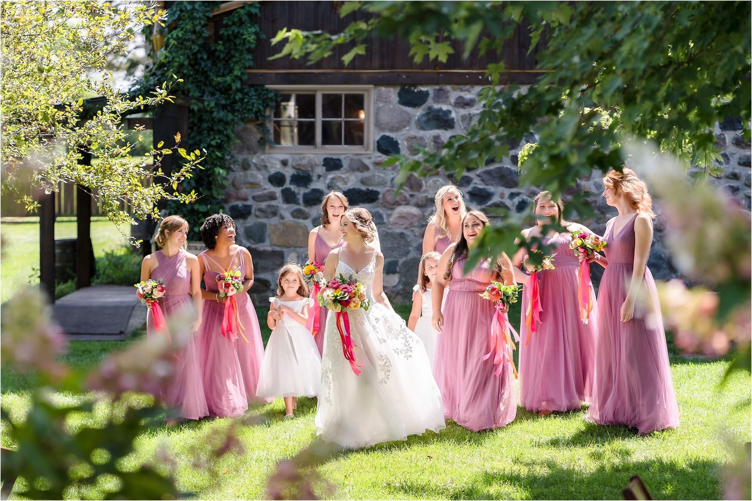  Backlit bridesmaids wearing pink dresses walk excitedly to their portrait location.  