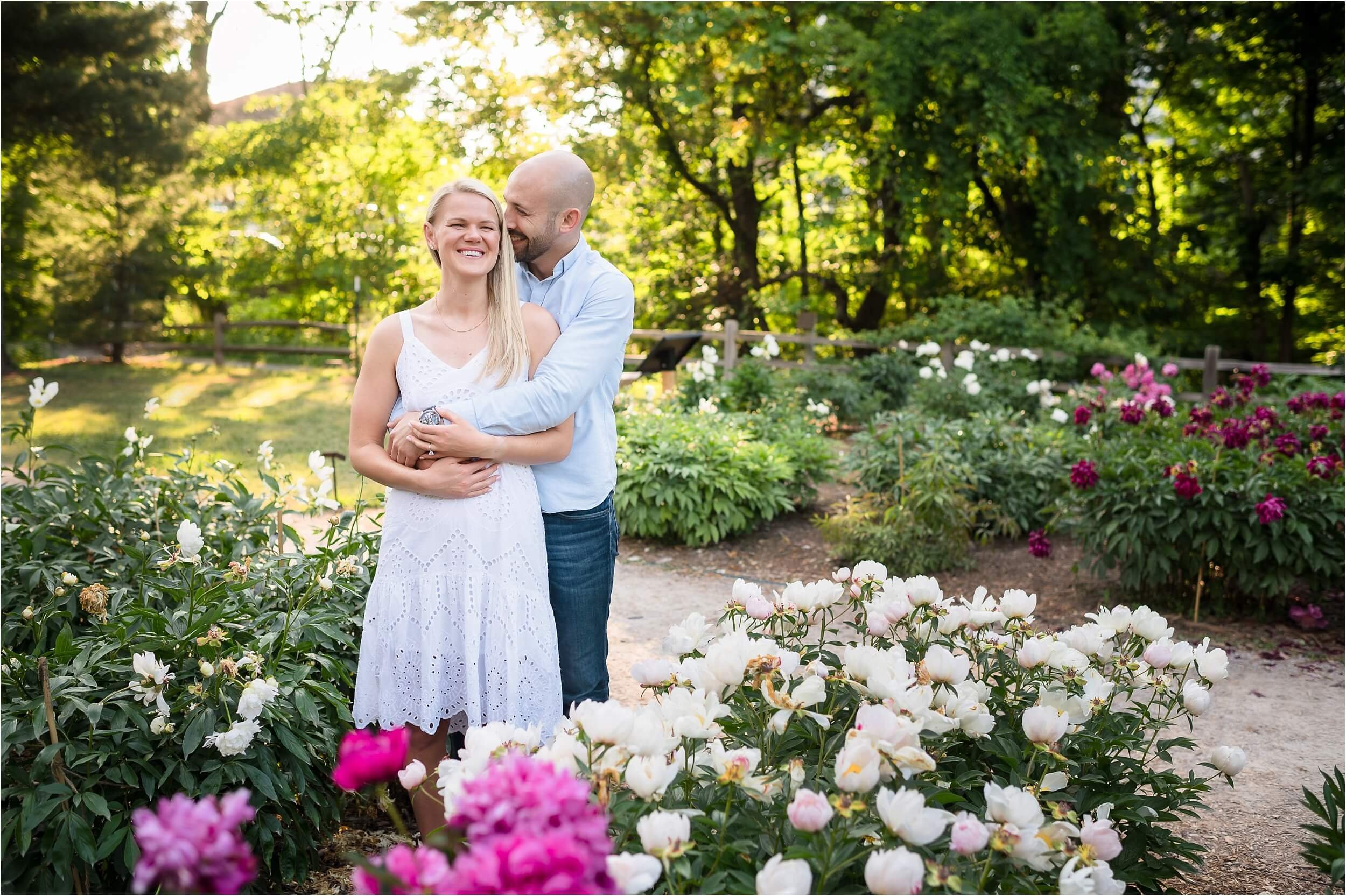  A couple laughs together during their portrait session in a lush garden.  