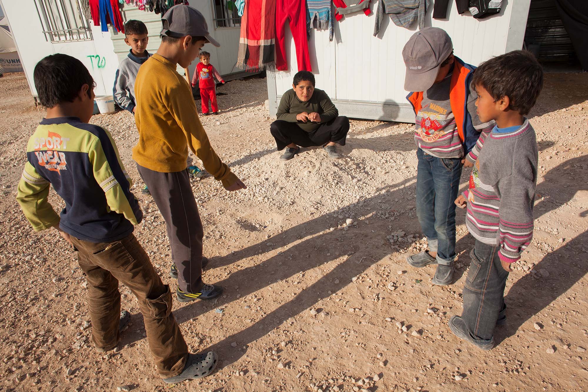  Syrian boys play marbles in the sand at Zaatari. Forms of social release and entertainment from the drudgery of living in the camp can be limited. One of the reasons that Clowns Without Borders have proven such a popular organization for children in