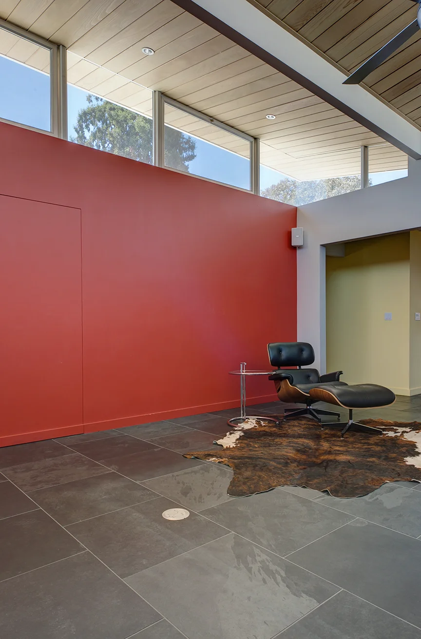 The bold red wall accentuates the atrium's floating roof. The use of strong primary colors is balanced out by neutral grays, and the natural wood ceiling. 