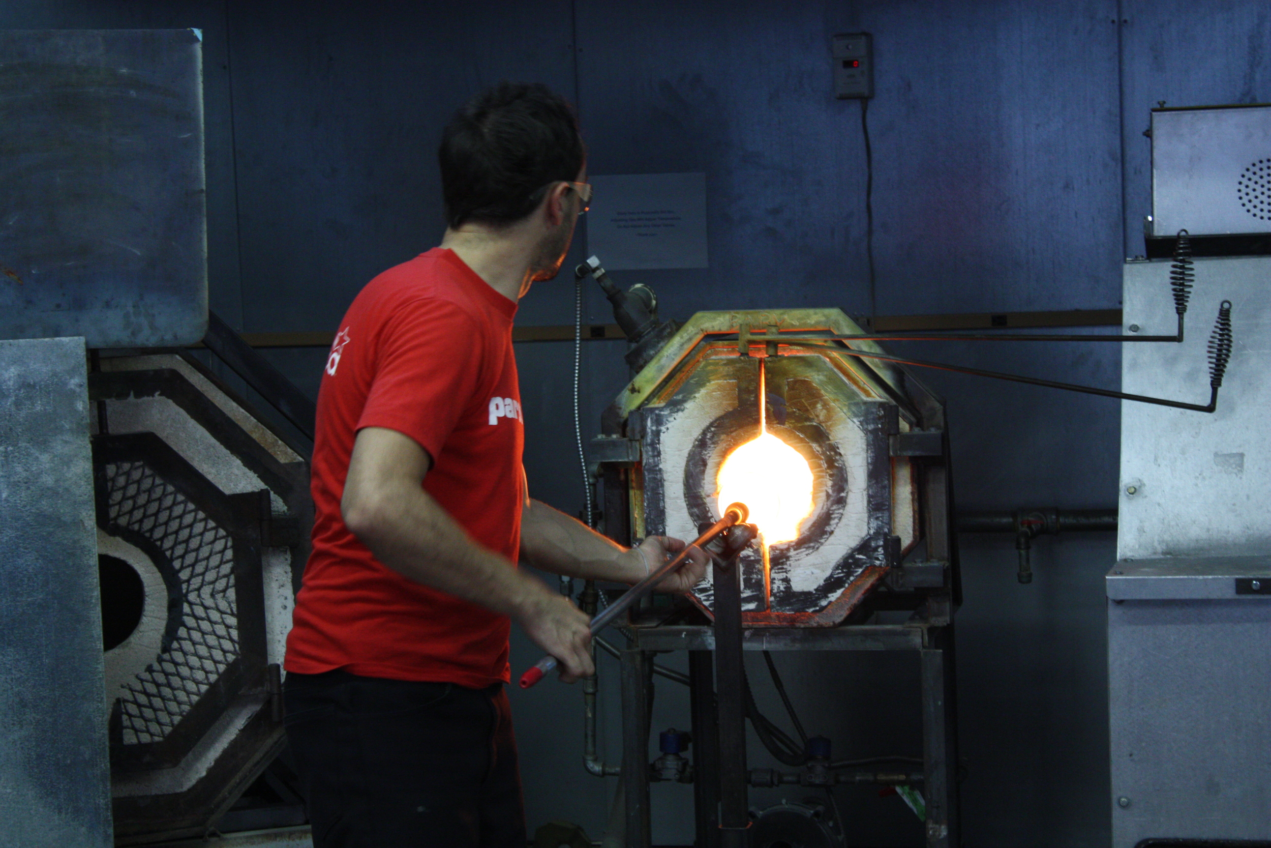   Here Esteban is heating the piece to keep it pliable for final adjustments, and checking the piece to see if it is done. He spent a lot of time heating the pieces in the furnace (also called a&nbsp;  glory hole  ). There are two different furnaces 
