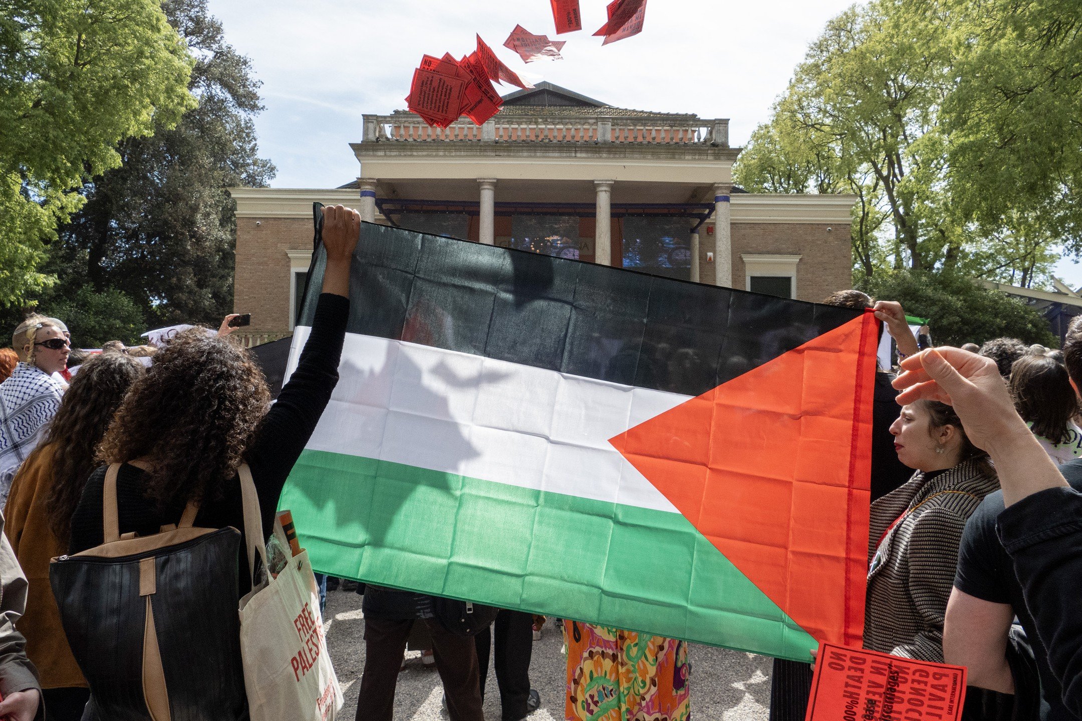 Venice, Italy, 17th April 2024 Amidst the serene Biennale Giardini, Palestinian protesters and supporters stand firm, voicing their stance. In front of the Israel, British, and German pavilions, the shadow of their cause is cast on their flag as red 