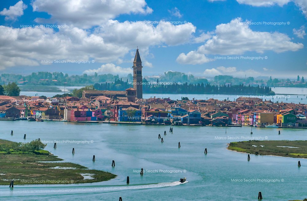 Island Palette: Burano as Seen from Torcello's Heights &ndash; This breathtaking view from the Campanile of the Abbazia in Torcello captures the essence of Burano's charm. The vibrant tapestry of colourful houses, contrasted with the serene blues of 