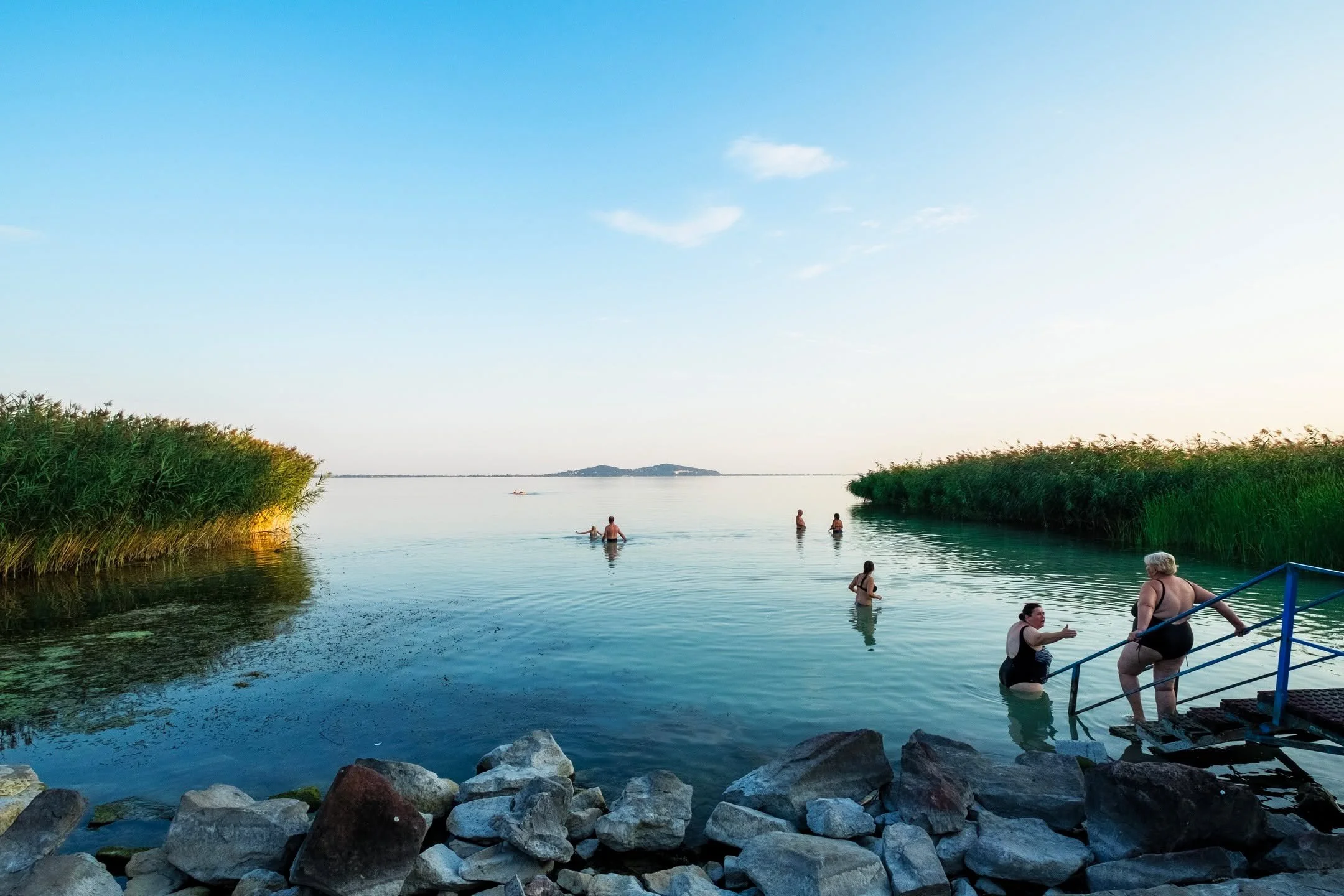 A summer evening at Lake Balaton, where the light turns soft and the air is still. Families wade into the calm water framed by reeds, while the horizon fades into pastel tones. Shot with Leica on Provia, a film that holds the warmth and quiet of thes