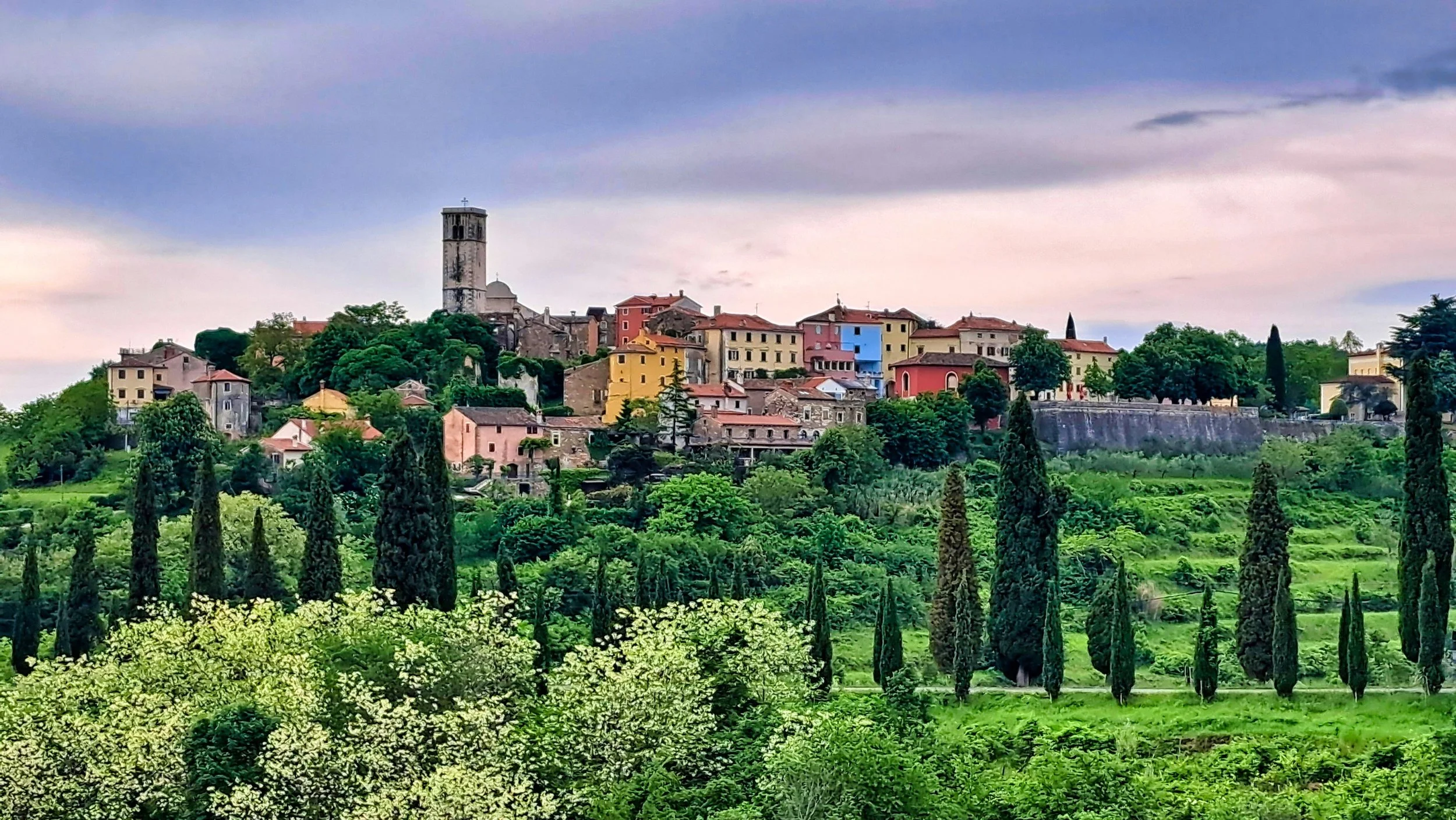 Some places do not try to impress you immediately.
They wait quietly behind a bend in the road, under a changing sky, surrounded by cypress trees and spring green so intense it almost feels painted.

That was my feeling arriving in Oprtalj today.

A 