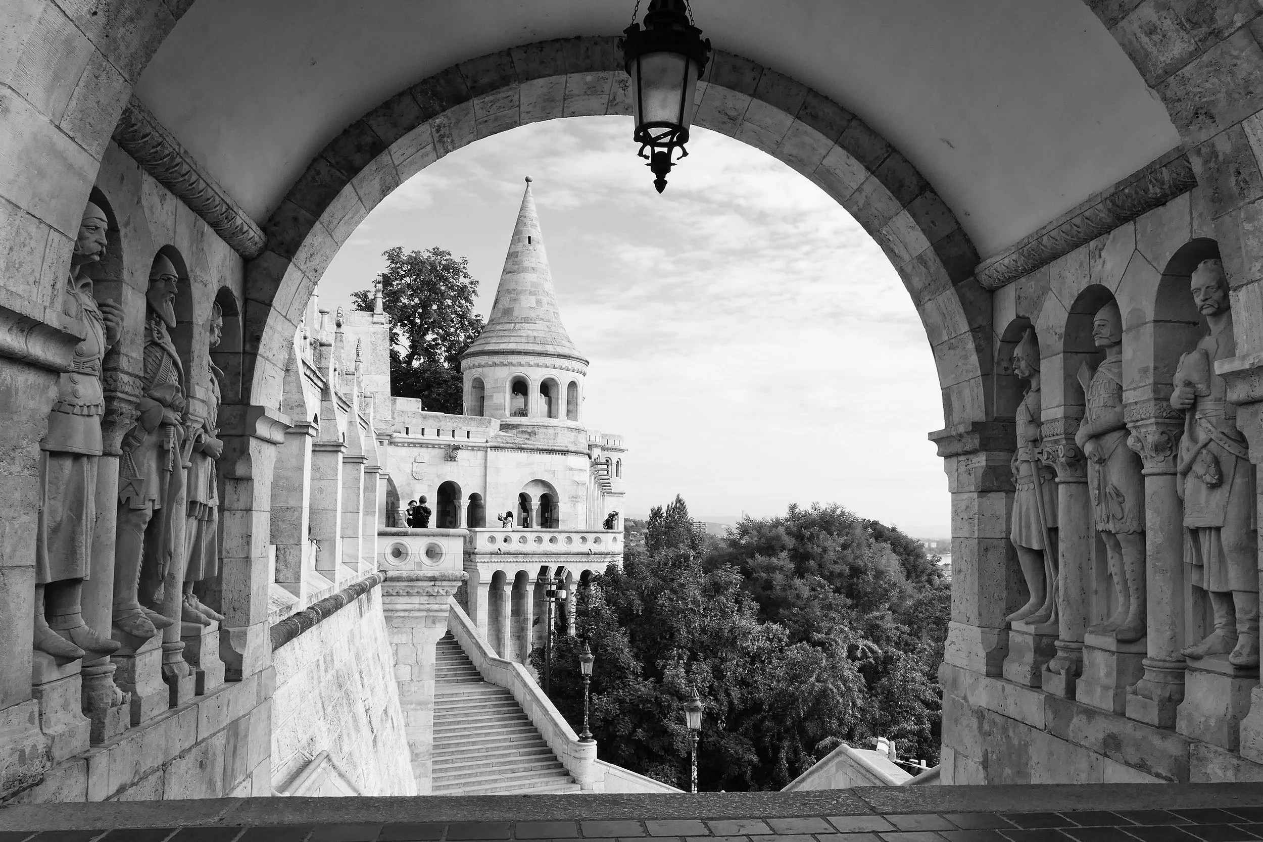 In Budapest, history is never quite behind you.

At Fisherman&rsquo;s Bastion, the old stone guardians remain in shadow while the city opens beyond the arch. The tower catches the eye first, but it is the figures watching silently from both sides tha