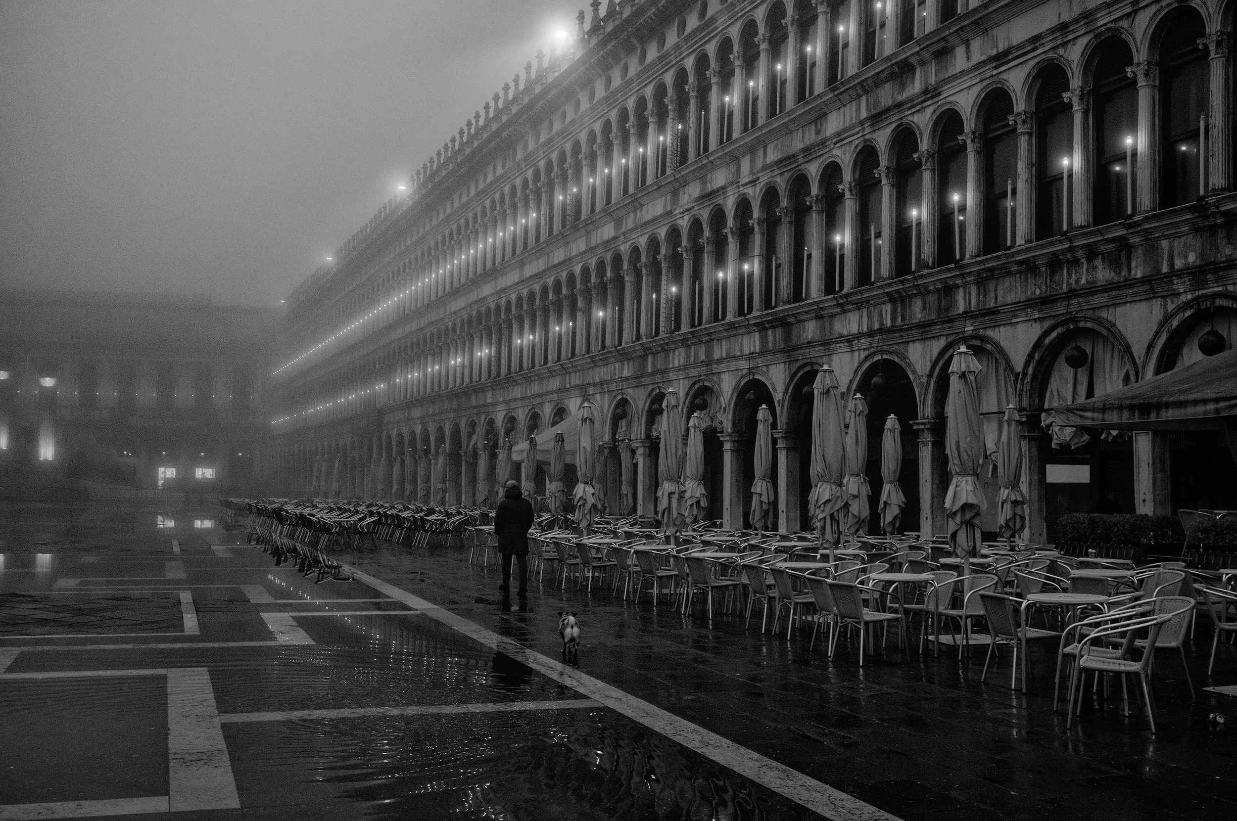 Venice was barely awake. Fog had swallowed the far end of Piazza San Marco, the caf&eacute;s were still closed, and their empty chairs waited beneath folded umbrellas. Then a solitary walker and a small dog entered the frame, giving scale to the sile