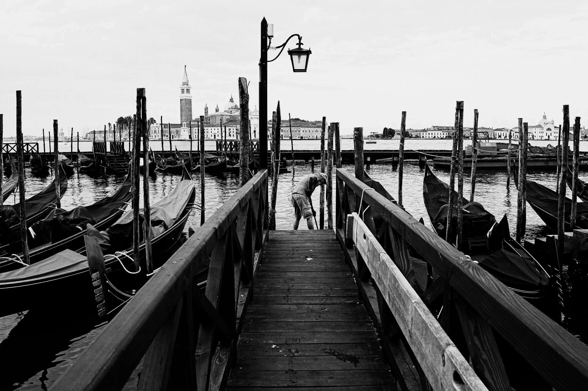 Venice gives you the backdrop. The people give you a reason to keep looking. Among the gondolas, mooring poles and familiar skyline, it&rsquo;s the bent figure at the end of the jetty that holds my attention. A small human gesture gives all that arch