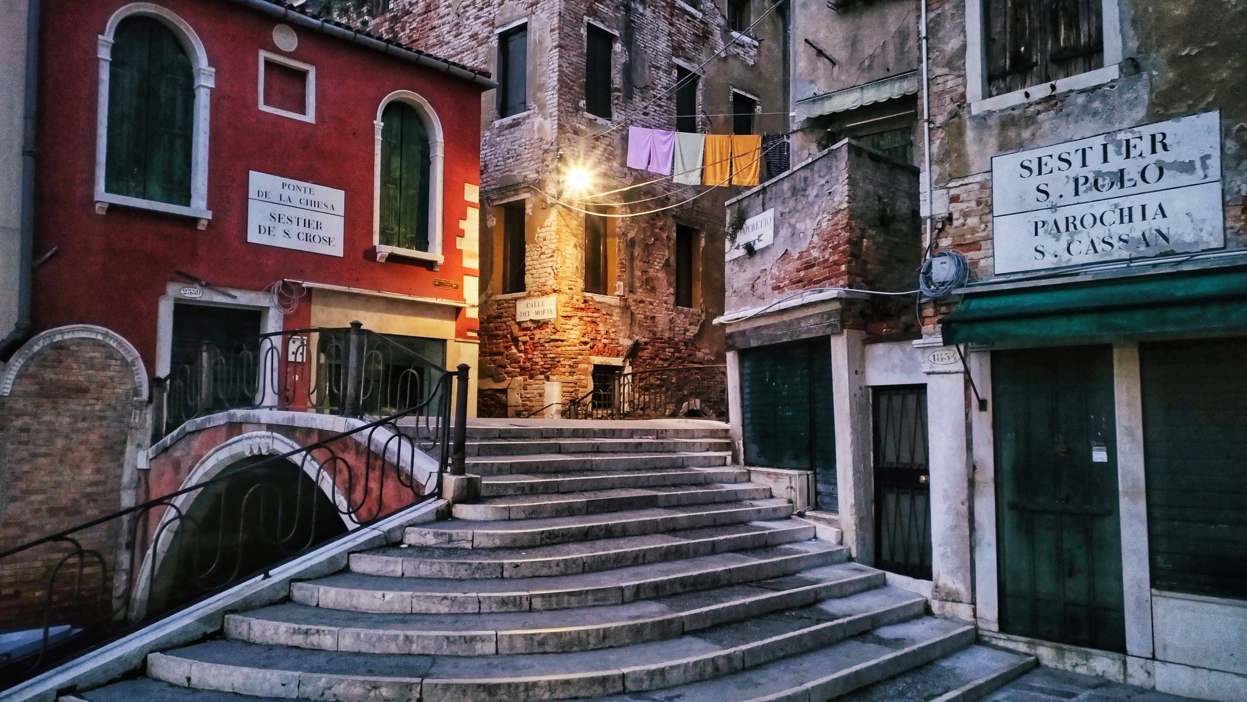 Venice, with nobody in the frame and someone&rsquo;s life just above it. The steps draw the eye towards the light, but the washing strung between the buildings gives this photograph its human presence. For me, those ordinary details often make a plac