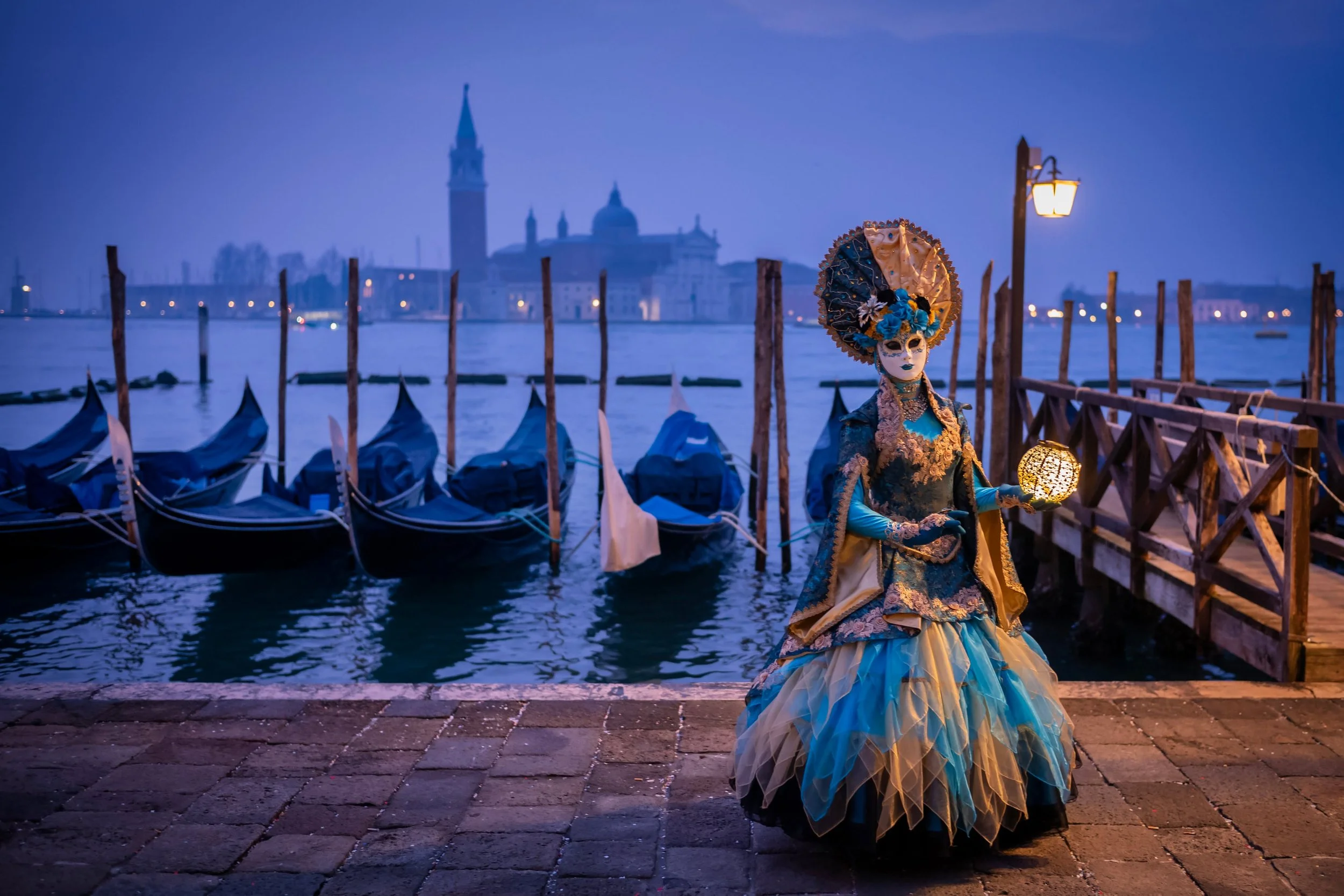 Before the first daylight reaches the waterfront, Venice Carnival is already awake. A costume appears beside the gondolas; another beneath the Piazzetta lamps. Against the lagoon's blue, even a small patch of red can hold the whole photograph togethe