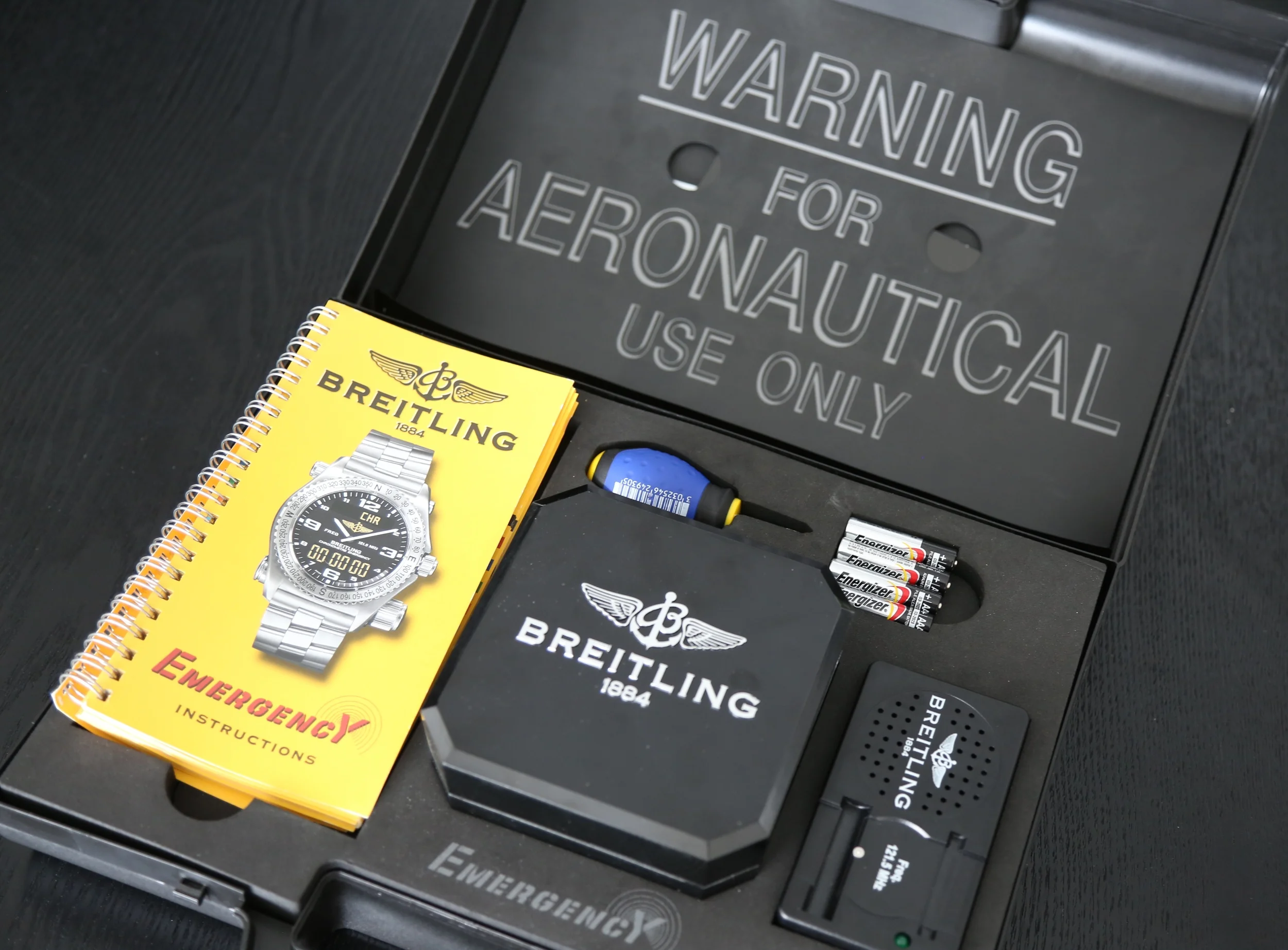 The Emergency watch comes in a plastic briefcase complete with large text warning label and test box, the test box is used to ensure the emergency beacon is still functioning. The original 1993 model was sold with a VHS instruction video that was later updated to a printed version. The blue rubberized screwdriver is a (superior) replacement, the original version was a plastic light grey colour.