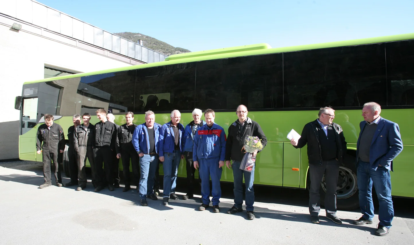 Dei tilsette med den første bussen som er blitt lakkert i den nye lakkhallen.