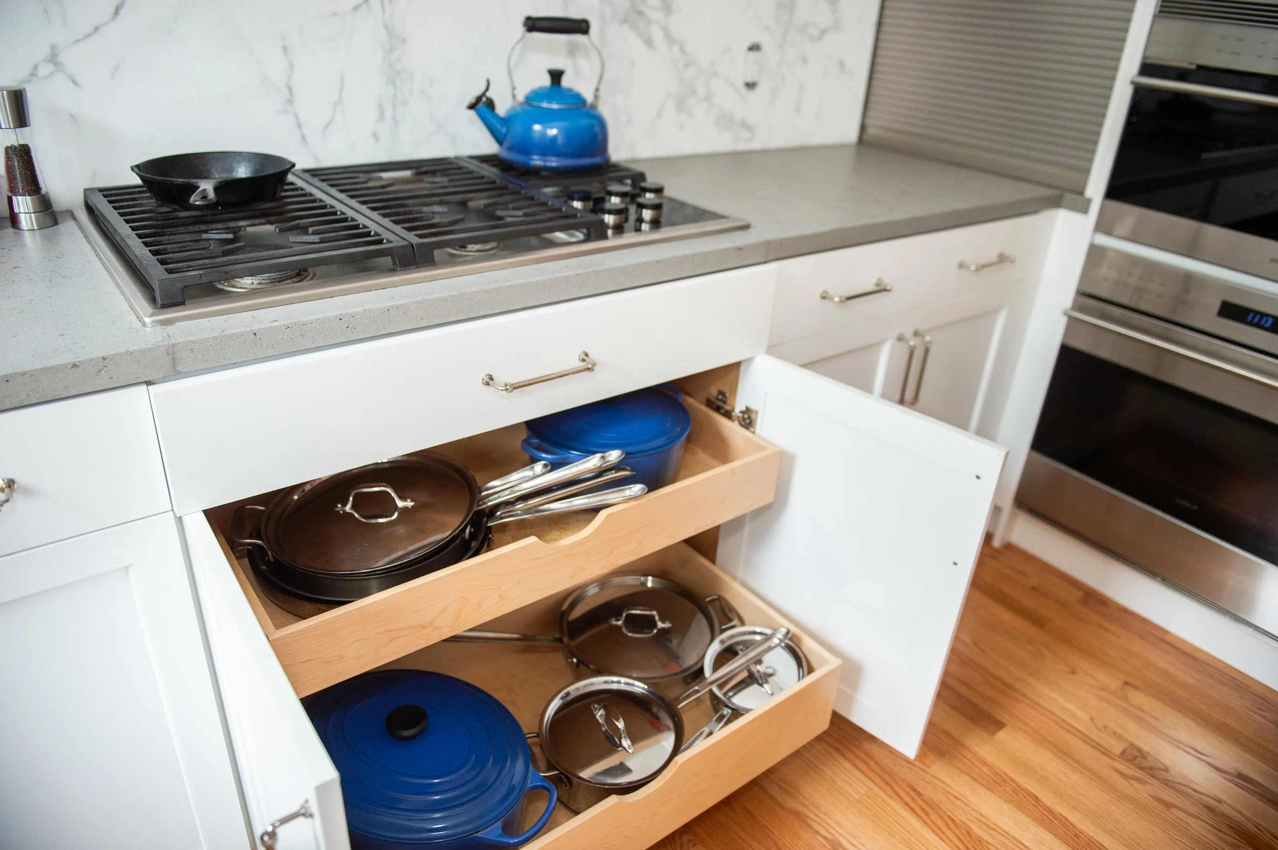 gray and white kitchen with pull out drawers below stove top for pots and pans
