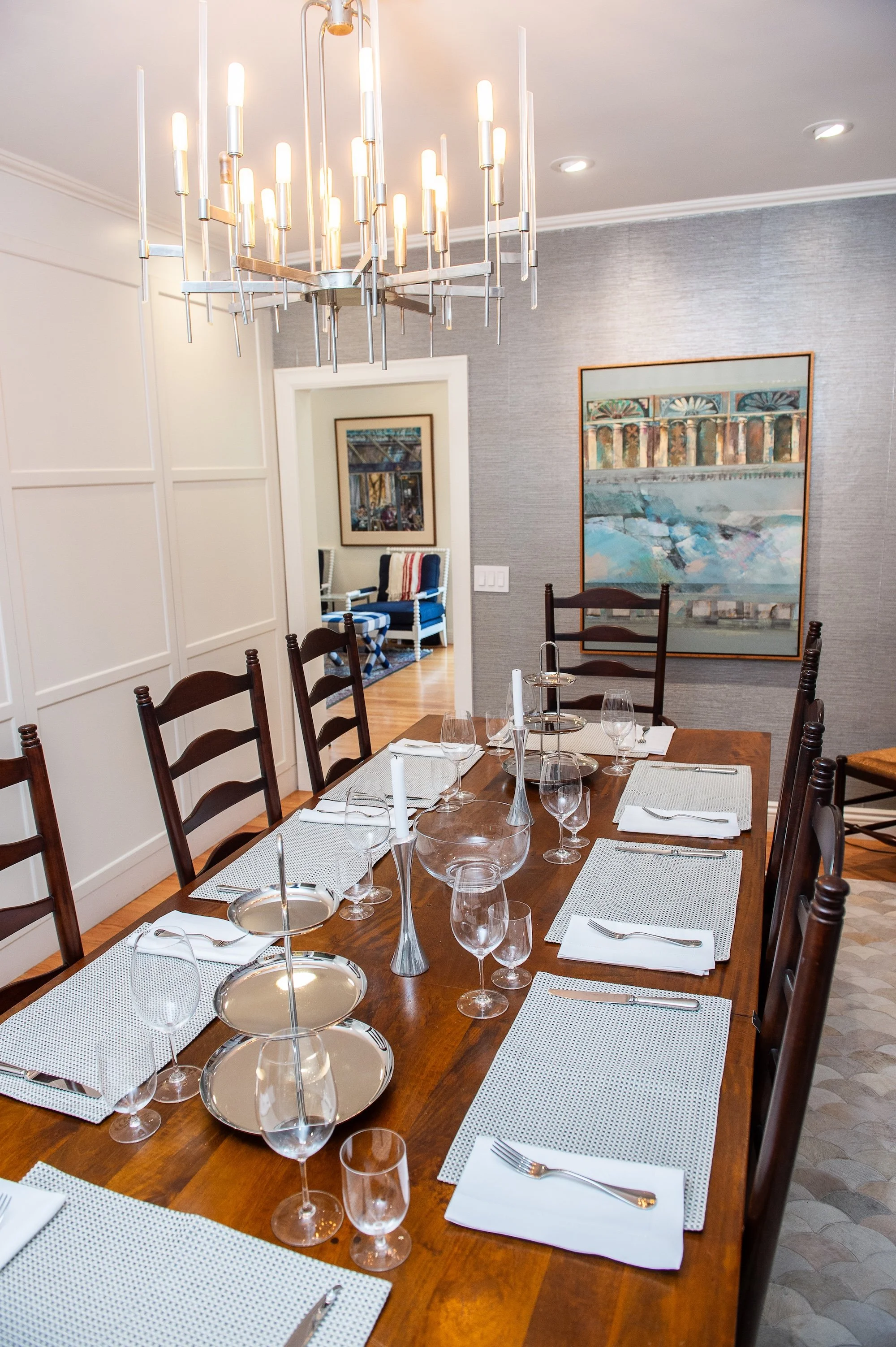 A wood dining room table with ladder back chairs is set for a party with silk placemats and chrome and glass accents
