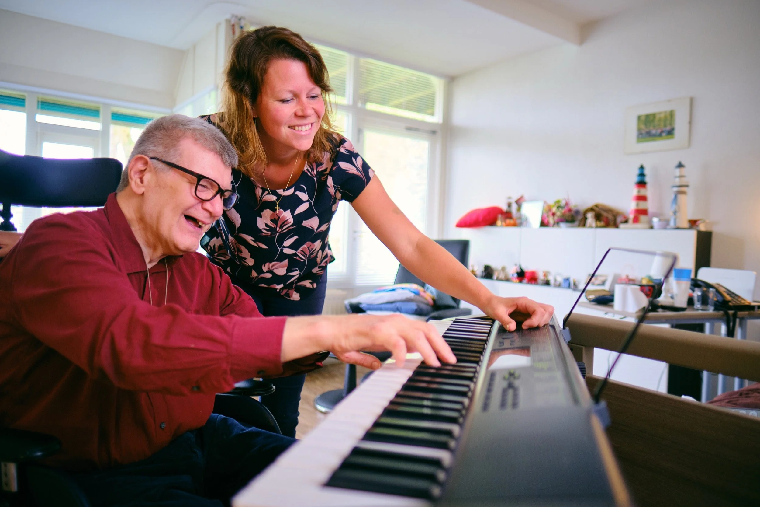 Een man en een vrouw spelen samen op een keyboard in een woonkamer, lachen en genieten van het moment.