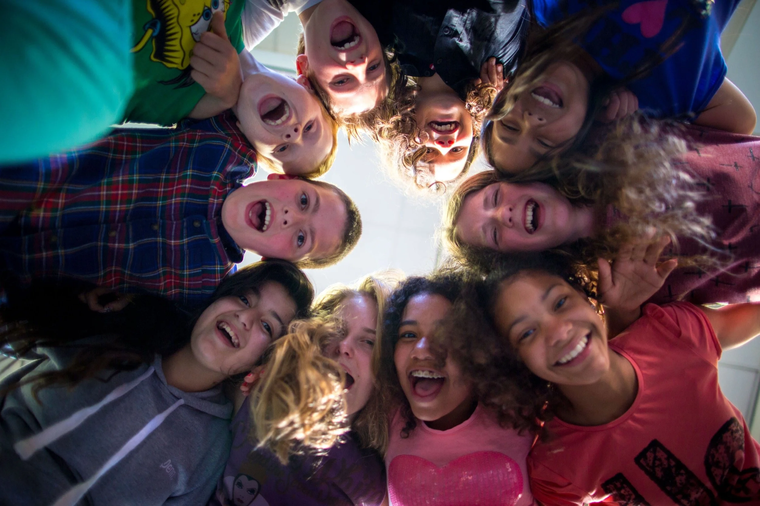 Een groep kinderen die in een cirkel naar beneden kijkt, lachend en met open monden