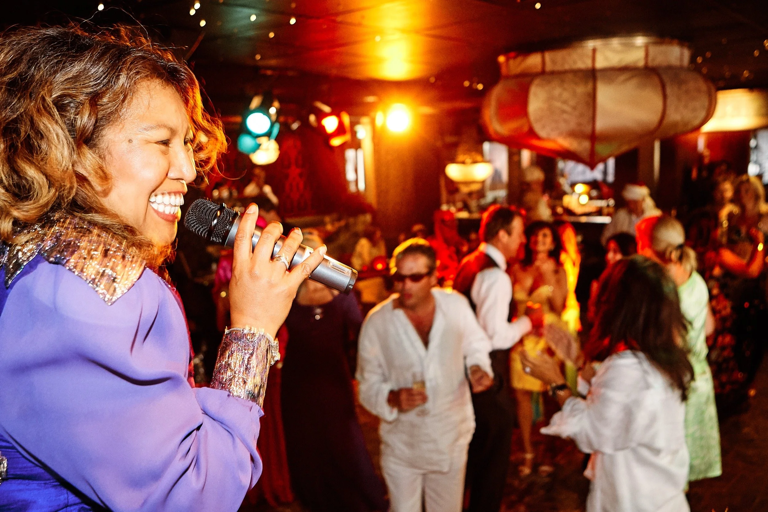 Vrolijke vrouw zingt in een kleurrijk, druk feest met veel mensen die dansen en feestvieren.