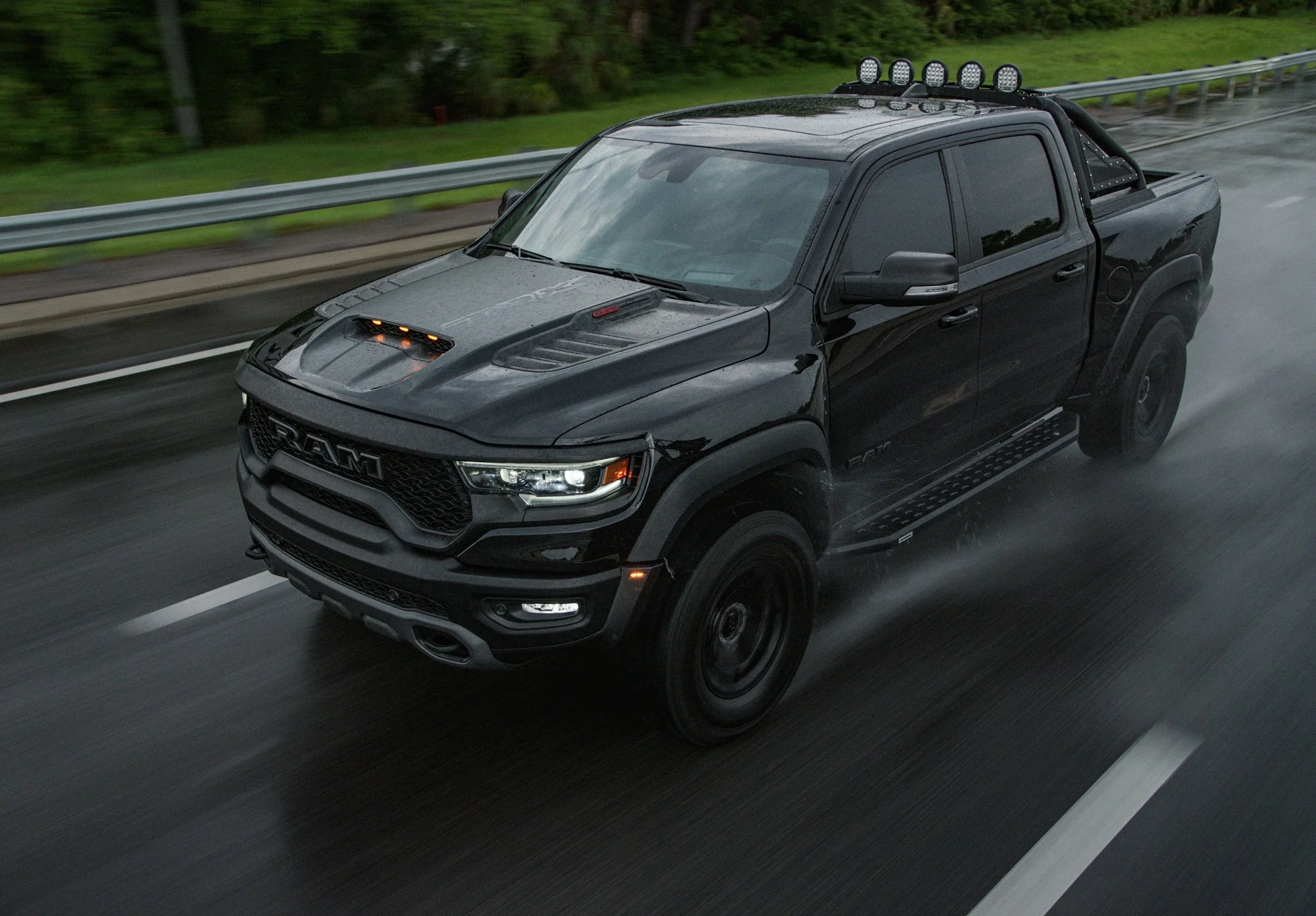A black Dodge Ram pickup truck driving on a wet road in rainy weather.